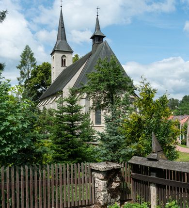 Zdjęcie nr 7: Kościół św. Antoniego Padewskiego w Trybszu jest usytuowany w centrum wsi, na południe od głównej drogi prowadzącej z Łapsz Wyżnych do Nowego Targu. Teren przykościelny jest otoczony wysokim murem, częściowo żeliwnym na kamiennej podmurówce, częściowo murowanym nakrytym cementowym daszkiem. Wejście od strony wschodniej oraz zachodniej przez szerokie bramy.

Kościół jest orientowany, murowany, otynkowany, jednonawowy z czworoboczną wieżą w fasadzie z prezbiterium zamkniętym trójbocznie. Dwuprzęsłowe prezbiterium oddziela od nawy szeroka ściana arkady tęczowej, zamknięte ostrołukowo. Nawa jest szersza i dłuższa, pięcioprzęsłowa. Wnętrze artykułowane jest dużymi i szerokimi oknami w kształcie stojących prostokątów, zamkniętych ostrołukowo, wypełnionych witrażami. Od południa do nawy przylega niewielka kruchta, a do prezbiterium od północy zakrystia. Na zachodniej ścianie nawy chór muzyczny wsparty na dwóch filarach, dostępny schodami od południowej strony nawy. Do kościoła prowadzi główne wejście od strony zachodniej oraz dwa mniejsze od strony południowej przez kruchtę i od strony północnej przez zakrystię.

W zewnętrznej elewacji kościoła widoczny jest niewysoki cokół, powyżej kościół otynkowany. Prezbiterium, o tej samej wysokości co nawa, lecz węższe z sygnaturką zwieńczoną iglicą. Nawa i prezbiterium oszkarpowane, nakryte dachem dwuspadowym. Do zachodniej fasady kościoła dostawiona jest wysoka założona na planie kwadratu wieża-dzwonnica. W dolnej kondygnacji na osi kościoła prostokątne wejście do kruchty, flankowane dwiema szkarpami. Fasada wieży w całości pokryta blachą, przechodzącą nad głównym wejściem do kościoła w daszek. Wieża zwieńczona iglicą.
