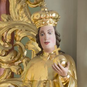 Zdjęcie nr 1: Rzeźba przedstawia nierozpoznanego świętego królewicza węgierskiego, ustawionego na półkolistym, srebrzonym cokole. Święty ukazany frontalnie, w lewej dłoni trzyma jabłko królewskie, a prawą, ugiętą w łokciu wyciąga do trzymania niezachowanego atrybutu. Twarz pełna, pulchna w dolnej części, o delikatnie rozchylonych ustach i dużych oczach. Głowa okolona długimi, ciemnobrązowymi włosami, zawiniętymi w duże loki do tyłu. Święty ubrany w spodnie, wysokie buty z cholewami, tunikę, pas i płaszcz, na głowie ma założoną mitrę książęcą. Draperia szat zaznaczona tylko przy rękawach; dłonie wyrzeźbione sztywno i niedbale. Polichromia w odsłoniętych partiach ciała naturalistyczna, szaty i atrybuty złocone oraz srebrzone.


