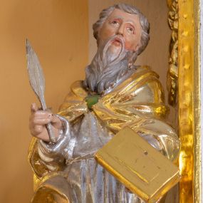 Zdjęcie nr 1: Rzeźba przedstawia świętego ewangelistę ustawionego na półkolistym, brązowym cokole. Święty ukazany frontalnie o delikatnie esowato wygiętej sylwetce. W prawej dłoni trzyma pióro, a w lewej księgę. Twarz o idealizowanych rysach, nos długi i prosty, wzrok wzniesiony ku górze. Głowa okolona długą i siwą brodą oraz siwymi, średniej długości włosami. Święty ubrany jest w srebrzoną suknię oraz złocony płaszcz, spięty na piersi zieloną klamrą, na stopach ma założone złocone buty. Draperia szat bujna o silnie falującym brzegu płaszcza. Polichromia w odsłoniętych partiach ciała naturalistyczna, szaty i atrybuty złocone oraz srebrzone.