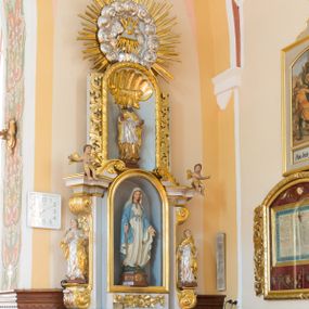 Zdjęcie nr 1: Ołtarz architektoniczny, dwukondygnacyjny, jednoosiowy ze zwieńczeniem. Ołtarz prostopadłościenny z drewnianą mensą i kamiennym portatylem. Antependium ozdobione trzema płycinami z czego środkowa w kształcie czwórliścia przenikającego się z kwadratem; dwie boczne, ustawione antytetycznie, w kształcie leżącego prostokąta z parą boków wewnętrznych w kształcie łuku nadwieszonego wklęsłego. W płycinie środkowej polichromowany monogram maryjny, w płycinach bocznych po lewej stronie Zwiastowanie, a po prawej Ucieczka do Egiptu. 

Nastawa na niewysokim, uskokowym cokole o ukośnie ustawionych bokach, zdobionych słonecznikami. W środkowej partii cokołu wkomponowane tabernakulum w formie prostopadłościennej szafki na profilowanym, uskokowym cokole z narożami ujętymi dwoma parami pilastrów z półwałkiem pośrodku trzonu, wspierających profilowany, uskokowy gzyms. Drzwiczki tabernakulum w kształcie prostokąta zamkniętego łukiem półkolistym, w polu płaskorzeźbiony kielich z Hostią oraz kłosami zbóż. Kondygnacja flankowana parą zdwojonych pilastrów oraz dostawionych, ustawionych pod kątem pilastrów z nałożonymi spływami wolutowymi. Podpory wspierają przerywane, niepełne belkowanie oraz przyczółek. Pole środkowe zajmuje wnęka w kształcie stojącego prostokąta, zamkniętego półkoliście. W polu figura Matki Boskiej Niepokalanie Poczętej. Pod wnęką podwieszona, rzeźbiona girlanda. Po lewej stronie kondygnacji, na cokole ułożonym na zakończeniu woluty ustawiona jest rzeźba św. Jana Ewangelisty, a po drugiej stronie figura nierozpoznanej świętej. Na belkowaniu usadzona jest para aniołków. Druga kondygnacja w formie wnęki w kształcie stojącego prostokąta, zamkniętego półkoliście, flankowana po bokach filarami, ozdobionymi liśćmi akantu. W polu umieszczona rzeźba św. Mikołaja. Nad rzeźbą stylizowana duża muszla palmetowa z podwieszonymi liśćmi akantu. Zwieńczenie w formie promienistej glorii z Okiem Opatrzności pośrodku, ujętej wieńcem srebrzonych obłoków. Struktura polichromowana na biało, detal architektoniczny i ornamentyka złocone oraz srebrzone. Na cokole tabliczka z napisem: „FUNDACJA / SREBRZENIE ŚWIECZNIKÓW / OŁTARZA NMP / Franciszek i Małgorzata Łojek / 2003”. 