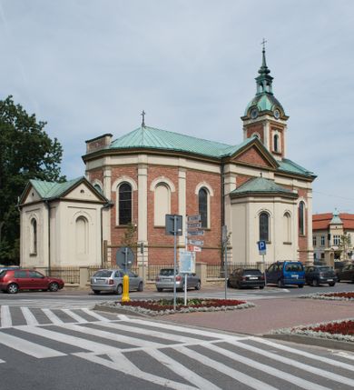 Zdjęcie nr 33: Kościół murowany, jednonawowy, z węższym prezbiterium zamkniętym trójbocznie oraz z wieżą wbudowaną w zachodnią fasadę. Do prezbiterium od północy przylega zakrystia, do nawy dwie kaplice leżące po przeciwległych stronach, zamknięte trójbocznie, od zachodu chór wsparty na dwóch filarach, z trójczęściową balustradą wychodzącą do przodu. Korpus trójprzęsłowy, przęsła oddzielone opilastrowanymi filarami podtrzymującymi arkady sklepienia. Nad kaplicami i prezbiterium fragmenty sklepienia gwiaździstego, nad nawą żaglaste. Wielobarwna polichromia  ścian i sklepień wypełnia podziały wyznaczone przez elementy architektoniczne, opiera się na motywach geometrycznych, stylizowanych floralnych, zoomorficznych i postaciach aniołów i świętych . Wszystkie okna w kształcie stojącego prostokąta zamkniętego półkoliście, w większości witraże, dwa w prezbiterium, po trzy z każdej strony nawy, po dwa w kaplicach, dwa na wysokości chóru, cztery w kondygnacji wieży; wyjątek stanowi okulus w fasadzie. Główne wejście przez fasadę, kolejne do zakrystii. Fasada dwukondygnacyjna, trójosiowa, na cokole, z wieżą. Osie wydzielone pilastrami, z których środkowa mieści drzwi o wykroju prostokąta i okulus w czworobocznej płycinie, a boczne zamknięte konchowo nisze w figurami św. Piotra po lewej i św. Pawła po prawej stronie. Kondygnacja zamknięta zdwojonym przyczółkiem. Wewnętrzny przerwany na kartusz herbowy i okrągłą plakietę z krzyżem, zewnętrzny na kondygnację wieży.  Wieża z każdej strony przepruta oknem zwieńczonym fragmentem gzymsu, na narożach ujęta pilastrami podtrzymującymi belkowanie z linią gzymsu wyoblającą się w środku i ujmującą tarczę zegara. Pozostałe elewacje na kamiennym cokole, nawa i prezbiterium z nietynkowanej cegły, kaplice i zakrystia otynkowane. Kontynuują podziały  pilastrami, artykulację podkreślają okna.  Dach nad nawą główną dwuspadowy, nad kaplicami i prezbiterium wieloboczne, wieża przekryta hełmem z latarnią, zwieńczona ostrosłupem z krzyżem.  
Najcenniejszym zabytkiem świątyni jest ołtarz główny z około 1700 roku przeniesiony tutaj z kościoła z Limanowej, interesująca jest polichromia o inspiracjach młodopolskich z elementami art  decó. 
