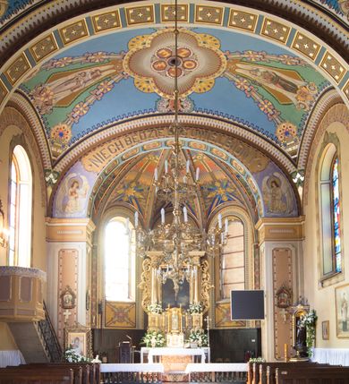 Zdjęcie nr 20: Kościół murowany, jednonawowy, z węższym prezbiterium zamkniętym trójbocznie oraz z wieżą wbudowaną w zachodnią fasadę. Do prezbiterium od północy przylega zakrystia, do nawy dwie kaplice leżące po przeciwległych stronach, zamknięte trójbocznie, od zachodu chór wsparty na dwóch filarach, z trójczęściową balustradą wychodzącą do przodu. Korpus trójprzęsłowy, przęsła oddzielone opilastrowanymi filarami podtrzymującymi arkady sklepienia. Nad kaplicami i prezbiterium fragmenty sklepienia gwiaździstego, nad nawą żaglaste. Wielobarwna polichromia  ścian i sklepień wypełnia podziały wyznaczone przez elementy architektoniczne, opiera się na motywach geometrycznych, stylizowanych floralnych, zoomorficznych i postaciach aniołów i świętych . Wszystkie okna w kształcie stojącego prostokąta zamkniętego półkoliście, w większości witraże, dwa w prezbiterium, po trzy z każdej strony nawy, po dwa w kaplicach, dwa na wysokości chóru, cztery w kondygnacji wieży; wyjątek stanowi okulus w fasadzie. Główne wejście przez fasadę, kolejne do zakrystii. Fasada dwukondygnacyjna, trójosiowa, na cokole, z wieżą. Osie wydzielone pilastrami, z których środkowa mieści drzwi o wykroju prostokąta i okulus w czworobocznej płycinie, a boczne zamknięte konchowo nisze w figurami św. Piotra po lewej i św. Pawła po prawej stronie. Kondygnacja zamknięta zdwojonym przyczółkiem. Wewnętrzny przerwany na kartusz herbowy i okrągłą plakietę z krzyżem, zewnętrzny na kondygnację wieży.  Wieża z każdej strony przepruta oknem zwieńczonym fragmentem gzymsu, na narożach ujęta pilastrami podtrzymującymi belkowanie z linią gzymsu wyoblającą się w środku i ujmującą tarczę zegara. Pozostałe elewacje na kamiennym cokole, nawa i prezbiterium z nietynkowanej cegły, kaplice i zakrystia otynkowane. Kontynuują podziały  pilastrami, artykulację podkreślają okna.  Dach nad nawą główną dwuspadowy, nad kaplicami i prezbiterium wieloboczne, wieża przekryta hełmem z latarnią, zwieńczona ostrosłupem z krzyżem.  
Najcenniejszym zabytkiem świątyni jest ołtarz główny z około 1700 roku przeniesiony tutaj z kościoła z Limanowej, interesująca jest polichromia o inspiracjach młodopolskich z elementami art  decó. 
