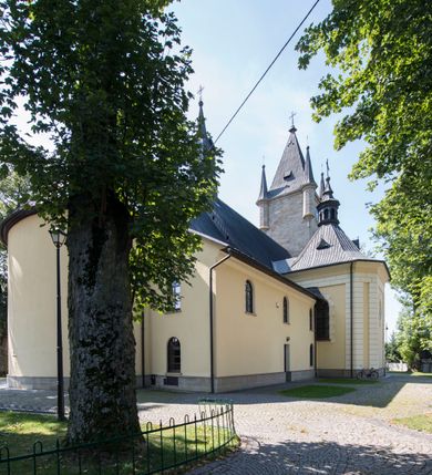 Zdjęcie nr 4: Kościół św. Andrzeja Apostoła w Szaflarach jest murowaną świątynią orientowaną. Składa się z czteroprzęsłowej nawy, przylegającego do niej od wschodu węższego, trójprzęsłowego prezbiterium zamkniętego łukiem spłaszczonym oraz czworobocznej wieży usytuowanej od zachodu. Po bokach nawy, na planie kwadratu ze ściętymi narożami, wzniesiono naprzeciw siebie dwie kaplice boczne, otwarte do wnętrza kościoła półokrągłymi arkadami. Od wschodu do kaplicy Najświętszego Serca Pana Jezusa przylega niewielka kruchta. Z kolei po stronie północnej prezbiterium wzniesiono na planie prostokąta zakrystię, poprzedzoną przedsionkiem i aneksem łączącym ją z kaplicą boczną Matki Boskiej, nad którym znajduje się skarbczyk. Prezbiterium doświetlone zostało przez trzy półokrągłe okna w ścianie południowej. Nawa, opięta na zewnątrz przyporami, została nakryta sklepieniem żaglastym z gurtami, a jej wnętrze, podobnie jak w prezbiterium, rozczłonkowano półfilarami. Zarówno nawę jak i prezbiterium nakryto dachem siodłowym, pokrytym blachą miedzianą. Obie kaplice boczne zasklepiono ośmiodzielnym sklepieniem i przykryto dachem namiotowym, wieńcząc go wielobocznymi latarniami z krzyżem. Doświetlają je półokrągłe okna oraz okulus, umieszczony w ścianie ołtarzowej, zamurowany w kaplicy Najświętszego Serca Pana Jezusa i od zewnątrz wypełniony współczesną mozaiką z wyobrażeniem Chrystusa Pantokratora. Elewacje prezbiterium, nawy i kaplic potynkowano. Od strony zachodniej do nawy przylega dwupoziomowa, czworoboczna wieża. Jej ściany olicowano okładziną z piaskowca. Dolny poziom wieży wyznacza nieznaczny uskok. Tu w przyziemiu urządzono kruchtę, do której prowadzi półokrągły portal. Nad portalem widoczny jest okulus. Górny poziom przepruto z trzech stron półokrągłymi oknami wypełnionymi drewnianymi żaluzjami. Wieżę zwieńczono ostrosłupowym hełmem, pokrytym blachą miedzianą i zakończonym krzyżem, który wspiera się na profilowanym gzymsie koronującym. Zwieńczenie wieży zostało wzbogacone w narożach czterema nadwieszonymi na wspornikach wielobocznymi wieżyczkami z ostrosłupowymi hełmami, pomiędzy którymi z trzech stron umieszczono tarcze zegarowe.