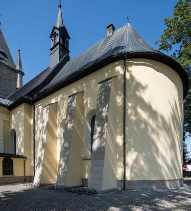 Zdjęcie nr 6: Kościół św. Andrzeja Apostoła w Szaflarach jest murowaną świątynią orientowaną. Składa się z czteroprzęsłowej nawy, przylegającego do niej od wschodu węższego, trójprzęsłowego prezbiterium zamkniętego łukiem spłaszczonym oraz czworobocznej wieży usytuowanej od zachodu. Po bokach nawy, na planie kwadratu ze ściętymi narożami, wzniesiono naprzeciw siebie dwie kaplice boczne, otwarte do wnętrza kościoła półokrągłymi arkadami. Od wschodu do kaplicy Najświętszego Serca Pana Jezusa przylega niewielka kruchta. Z kolei po stronie północnej prezbiterium wzniesiono na planie prostokąta zakrystię, poprzedzoną przedsionkiem i aneksem łączącym ją z kaplicą boczną Matki Boskiej, nad którym znajduje się skarbczyk. Prezbiterium doświetlone zostało przez trzy półokrągłe okna w ścianie południowej. Nawa, opięta na zewnątrz przyporami, została nakryta sklepieniem żaglastym z gurtami, a jej wnętrze, podobnie jak w prezbiterium, rozczłonkowano półfilarami. Zarówno nawę jak i prezbiterium nakryto dachem siodłowym, pokrytym blachą miedzianą. Obie kaplice boczne zasklepiono ośmiodzielnym sklepieniem i przykryto dachem namiotowym, wieńcząc go wielobocznymi latarniami z krzyżem. Doświetlają je półokrągłe okna oraz okulus, umieszczony w ścianie ołtarzowej, zamurowany w kaplicy Najświętszego Serca Pana Jezusa i od zewnątrz wypełniony współczesną mozaiką z wyobrażeniem Chrystusa Pantokratora. Elewacje prezbiterium, nawy i kaplic potynkowano. Od strony zachodniej do nawy przylega dwupoziomowa, czworoboczna wieża. Jej ściany olicowano okładziną z piaskowca. Dolny poziom wieży wyznacza nieznaczny uskok. Tu w przyziemiu urządzono kruchtę, do której prowadzi półokrągły portal. Nad portalem widoczny jest okulus. Górny poziom przepruto z trzech stron półokrągłymi oknami wypełnionymi drewnianymi żaluzjami. Wieżę zwieńczono ostrosłupowym hełmem, pokrytym blachą miedzianą i zakończonym krzyżem, który wspiera się na profilowanym gzymsie koronującym. Zwieńczenie wieży zostało wzbogacone w narożach czterema nadwieszonymi na wspornikach wielobocznymi wieżyczkami z ostrosłupowymi hełmami, pomiędzy którymi z trzech stron umieszczono tarcze zegarowe.