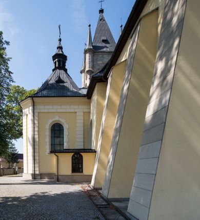 Zdjęcie nr 5: Kościół św. Andrzeja Apostoła w Szaflarach jest murowaną świątynią orientowaną. Składa się z czteroprzęsłowej nawy, przylegającego do niej od wschodu węższego, trójprzęsłowego prezbiterium zamkniętego łukiem spłaszczonym oraz czworobocznej wieży usytuowanej od zachodu. Po bokach nawy, na planie kwadratu ze ściętymi narożami, wzniesiono naprzeciw siebie dwie kaplice boczne, otwarte do wnętrza kościoła półokrągłymi arkadami. Od wschodu do kaplicy Najświętszego Serca Pana Jezusa przylega niewielka kruchta. Z kolei po stronie północnej prezbiterium wzniesiono na planie prostokąta zakrystię, poprzedzoną przedsionkiem i aneksem łączącym ją z kaplicą boczną Matki Boskiej, nad którym znajduje się skarbczyk. Prezbiterium doświetlone zostało przez trzy półokrągłe okna w ścianie południowej. Nawa, opięta na zewnątrz przyporami, została nakryta sklepieniem żaglastym z gurtami, a jej wnętrze, podobnie jak w prezbiterium, rozczłonkowano półfilarami. Zarówno nawę jak i prezbiterium nakryto dachem siodłowym, pokrytym blachą miedzianą. Obie kaplice boczne zasklepiono ośmiodzielnym sklepieniem i przykryto dachem namiotowym, wieńcząc go wielobocznymi latarniami z krzyżem. Doświetlają je półokrągłe okna oraz okulus, umieszczony w ścianie ołtarzowej, zamurowany w kaplicy Najświętszego Serca Pana Jezusa i od zewnątrz wypełniony współczesną mozaiką z wyobrażeniem Chrystusa Pantokratora. Elewacje prezbiterium, nawy i kaplic potynkowano. Od strony zachodniej do nawy przylega dwupoziomowa, czworoboczna wieża. Jej ściany olicowano okładziną z piaskowca. Dolny poziom wieży wyznacza nieznaczny uskok. Tu w przyziemiu urządzono kruchtę, do której prowadzi półokrągły portal. Nad portalem widoczny jest okulus. Górny poziom przepruto z trzech stron półokrągłymi oknami wypełnionymi drewnianymi żaluzjami. Wieżę zwieńczono ostrosłupowym hełmem, pokrytym blachą miedzianą i zakończonym krzyżem, który wspiera się na profilowanym gzymsie koronującym. Zwieńczenie wieży zostało wzbogacone w narożach czterema nadwieszonymi na wspornikach wielobocznymi wieżyczkami z ostrosłupowymi hełmami, pomiędzy którymi z trzech stron umieszczono tarcze zegarowe.