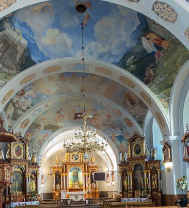 Zdjęcie nr 9: Kościół św. Andrzeja Apostoła w Szaflarach jest murowaną świątynią orientowaną. Składa się z czteroprzęsłowej nawy, przylegającego do niej od wschodu węższego, trójprzęsłowego prezbiterium zamkniętego łukiem spłaszczonym oraz czworobocznej wieży usytuowanej od zachodu. Po bokach nawy, na planie kwadratu ze ściętymi narożami, wzniesiono naprzeciw siebie dwie kaplice boczne, otwarte do wnętrza kościoła półokrągłymi arkadami. Od wschodu do kaplicy Najświętszego Serca Pana Jezusa przylega niewielka kruchta. Z kolei po stronie północnej prezbiterium wzniesiono na planie prostokąta zakrystię, poprzedzoną przedsionkiem i aneksem łączącym ją z kaplicą boczną Matki Boskiej, nad którym znajduje się skarbczyk. Prezbiterium doświetlone zostało przez trzy półokrągłe okna w ścianie południowej. Nawa, opięta na zewnątrz przyporami, została nakryta sklepieniem żaglastym z gurtami, a jej wnętrze, podobnie jak w prezbiterium, rozczłonkowano półfilarami. Zarówno nawę jak i prezbiterium nakryto dachem siodłowym, pokrytym blachą miedzianą. Obie kaplice boczne zasklepiono ośmiodzielnym sklepieniem i przykryto dachem namiotowym, wieńcząc go wielobocznymi latarniami z krzyżem. Doświetlają je półokrągłe okna oraz okulus, umieszczony w ścianie ołtarzowej, zamurowany w kaplicy Najświętszego Serca Pana Jezusa i od zewnątrz wypełniony współczesną mozaiką z wyobrażeniem Chrystusa Pantokratora. Elewacje prezbiterium, nawy i kaplic potynkowano. Od strony zachodniej do nawy przylega dwupoziomowa, czworoboczna wieża. Jej ściany olicowano okładziną z piaskowca. Dolny poziom wieży wyznacza nieznaczny uskok. Tu w przyziemiu urządzono kruchtę, do której prowadzi półokrągły portal. Nad portalem widoczny jest okulus. Górny poziom przepruto z trzech stron półokrągłymi oknami wypełnionymi drewnianymi żaluzjami. Wieżę zwieńczono ostrosłupowym hełmem, pokrytym blachą miedzianą i zakończonym krzyżem, który wspiera się na profilowanym gzymsie koronującym. Zwieńczenie wieży zostało wzbogacone w narożach czterema nadwieszonymi na wspornikach wielobocznymi wieżyczkami z ostrosłupowymi hełmami, pomiędzy którymi z trzech stron umieszczono tarcze zegarowe.