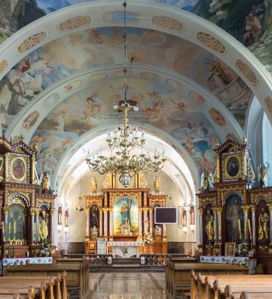 Zdjęcie nr 11: Kościół św. Andrzeja Apostoła w Szaflarach jest murowaną świątynią orientowaną. Składa się z czteroprzęsłowej nawy, przylegającego do niej od wschodu węższego, trójprzęsłowego prezbiterium zamkniętego łukiem spłaszczonym oraz czworobocznej wieży usytuowanej od zachodu. Po bokach nawy, na planie kwadratu ze ściętymi narożami, wzniesiono naprzeciw siebie dwie kaplice boczne, otwarte do wnętrza kościoła półokrągłymi arkadami. Od wschodu do kaplicy Najświętszego Serca Pana Jezusa przylega niewielka kruchta. Z kolei po stronie północnej prezbiterium wzniesiono na planie prostokąta zakrystię, poprzedzoną przedsionkiem i aneksem łączącym ją z kaplicą boczną Matki Boskiej, nad którym znajduje się skarbczyk. Prezbiterium doświetlone zostało przez trzy półokrągłe okna w ścianie południowej. Nawa, opięta na zewnątrz przyporami, została nakryta sklepieniem żaglastym z gurtami, a jej wnętrze, podobnie jak w prezbiterium, rozczłonkowano półfilarami. Zarówno nawę jak i prezbiterium nakryto dachem siodłowym, pokrytym blachą miedzianą. Obie kaplice boczne zasklepiono ośmiodzielnym sklepieniem i przykryto dachem namiotowym, wieńcząc go wielobocznymi latarniami z krzyżem. Doświetlają je półokrągłe okna oraz okulus, umieszczony w ścianie ołtarzowej, zamurowany w kaplicy Najświętszego Serca Pana Jezusa i od zewnątrz wypełniony współczesną mozaiką z wyobrażeniem Chrystusa Pantokratora. Elewacje prezbiterium, nawy i kaplic potynkowano. Od strony zachodniej do nawy przylega dwupoziomowa, czworoboczna wieża. Jej ściany olicowano okładziną z piaskowca. Dolny poziom wieży wyznacza nieznaczny uskok. Tu w przyziemiu urządzono kruchtę, do której prowadzi półokrągły portal. Nad portalem widoczny jest okulus. Górny poziom przepruto z trzech stron półokrągłymi oknami wypełnionymi drewnianymi żaluzjami. Wieżę zwieńczono ostrosłupowym hełmem, pokrytym blachą miedzianą i zakończonym krzyżem, który wspiera się na profilowanym gzymsie koronującym. Zwieńczenie wieży zostało wzbogacone w narożach czterema nadwieszonymi na wspornikach wielobocznymi wieżyczkami z ostrosłupowymi hełmami, pomiędzy którymi z trzech stron umieszczono tarcze zegarowe.