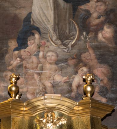 Zdjęcie nr 5: Nastawa ołtarzowa jednoosiowa, jednokondygnacyjna ze zwieńczeniem, ustawiona na wysokim dwustrefowym cokole, zryzalitowanym na zewnetrznych krawędziach. Ołtarz prostopadłościenny z kamienną mensą. Antepedium drewniane, dekorowane na wybrzuszeniu trzema płycinami z rytą wicią roślinną i monogramem IHS. Tabernakulum w kształcie kapliczki na cokole w formie prostopadłościanu; ścianka frontowa ujęta półfilarami dźwigającymi gzyms opasujący go z trzech stron, na froncie przyjmujący kształt łuku segmentowego, spiętego ustawionymi przeciwstawnie wolutami. Trzony półfilarów dekorowane owocowo-roślinnymi zwisami, pole środkowe skręconymi liśćmi akantu w układzie lustrzanym. Na nim nastawa w formie półokrągłej ścianki dekorowanej płyciną w kształcie stojącego prostokąta zamkniętego łukiem pełnym zdobionym kielichem z unoszącą się ponad nim hostią w otoczeniu promieni. Drzwiczki ujęte skręconymi kolumnami dźwigającymi pełne belkowanie wyłamane na ich osiach i wyniesione w łuk na polem centralnym. Na środku fryzu uskrzydlona główka anielska. Na wyłamanych częściach belkowania wazony płomieniste. Nastawa ołtarzowa ujęta parą kolumn o kapitelach kompozytowych dźwigających fragmenty belkowania o silnie wysuniętym gzymsie, połączone architrawem przyjmującym nad polem środkowym kształt łuku pełnego. Pole środkowe niemal w całości wypełnia nisza ujęta ramą w formie stojącego prostokąta wyłamanego prostokątnie w partii górnego boku, wypełniona obrazem św. Rodziny wymiennie z wizerunkiem Matki Boskiej Niepokalanie Poczętej. Zwieńczenie na zwężającej się łukowato podstawie w formie przyczółka przerwanego pośrodku cokołem z krzyżem. Cokół w górnej strefie dekorowany płycinami, w partii ryzalitów wypełnionymi akantem mięsistym i uskrzydloną główką anielską na froncie. Rama obrazu w polu środkowym dekorowana wstęgą i liśćmi; w prostokątnym polu nad obrazem płaskorzeźbione obłoki z rzeźbą Gołębicy Ducha Świętego w glorii; powyżej w polu łuku półpostać Boga Ojca z rozłożonymi na boki rękami. Kondygnacja ujęta uszakami utworzonymi z silnie skręcanego mięsistego akantu, zwiniętego w woluty oraz guzy. Krawędzie podstawy zwieńczenia oraz gzyms przyczółka dekorowane liśćmi akantu. Struktura polichromowana w kolorze kremowym; ornamentyka, profile i kolumny złocone i srebrzone.