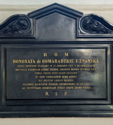 Zdjęcie nr 1: Płyta w kształcie leżącego prostokąta ujęta profilowaną ramą z uszakami, zwieńczona węższym, prostokątnym polem zamkniętym trójkątnym, profilowanym gzymsem, ujętym dwoma zwróconymi do siebie wolutami ze spływami wypełnionymi listkami. W polu kuta, złocona inskrypcja „D(EO) O(PTIMO) M(AXIMO) / HONORATA de DOMARADZKIE UZNAŃSKA / HERES BONORUM SZAFLARY * 12 JANUARII 1797. 28. APRILIS 1878. / IMITABILE EXEMPLAR CARAE UXORIS, AMANTIS MATRIS, OPTIMAE CIVIS, / VIDUA FACTA DUOS FILIOS EDUCAVIT, / ET REM FAMILIAREM BENE GESSIT. / EX SEPTEM LIBERIS QUINQUE / SUMMOS DIGNITATIS GRADUS OBTINUERUNT IN CIVITATE. / AD PERPETUAM MEMORIAM POSUIT GRATO ANIMO FILIUS. / R(EQUIESCAT) I(N) P(ACE)”.  
