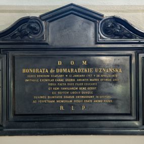 Zdjęcie nr 1: Płyta w kształcie leżącego prostokąta ujęta profilowaną ramą z uszakami, zwieńczona węższym, prostokątnym polem zamkniętym trójkątnym, profilowanym gzymsem, ujętym dwoma zwróconymi do siebie wolutami ze spływami wypełnionymi listkami. W polu kuta, złocona inskrypcja „D(EO) O(PTIMO) M(AXIMO) / HONORATA de DOMARADZKIE UZNAŃSKA / HERES BONORUM SZAFLARY * 12 JANUARII 1797. 28. APRILIS 1878. / IMITABILE EXEMPLAR CARAE UXORIS, AMANTIS MATRIS, OPTIMAE CIVIS, / VIDUA FACTA DUOS FILIOS EDUCAVIT, / ET REM FAMILIAREM BENE GESSIT. / EX SEPTEM LIBERIS QUINQUE / SUMMOS DIGNITATIS GRADUS OBTINUERUNT IN CIVITATE. / AD PERPETUAM MEMORIAM POSUIT GRATO ANIMO FILIUS. / R(EQUIESCAT) I(N) P(ACE)”.  

