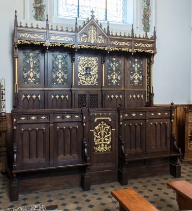 Zdjęcie nr 2: Dębowe, przyścienne stalle uzyskały formę neogotyckiej, pięcioosiowej struktury architektonicznej z zapleckiem i baldachimem. Całość wznosi się na wysokim postumencie. Wejście do nich prowadzi z boków oraz z przodu na osi centralnej, gdzie wprawiono drzwiczki. Ozdobiono je płaskorzeźbioną i złoconą ornamentalną wicią roślinną wpisaną w prostokątną płycinę zwieńczoną stylizowanym trójliściem. Ponad płyciną wprowadzono fryz lombardzki, a poniżej trzy mniejsze, prostokątne, puste płyciny. Na pozostałych osiach na przedpiersiu usytuowano cztery płyciny, które stanowią zaplecek dla dwóch ławek flankujących wejście środkowe. Ławki ujmują wolutowe boki, zdobione stylizowanymi liśćmi akantu, przechodzące poniżej na dekoracyjne wsporniki ustawione na wysokich cokolikach. Jednocześnie wolutowe boki przylegają do wysokich postumentów, na których ustawiono kolumienki o złoconych kapitelach korynckich, podtrzymujących wyłamane belkowanie, stanowiące jednocześnie parapet stalli. Każdą z dolnych płycin zdobi triada półokrągłych arkadek wspartych na smukłych kolumienkach ustawionych na cokole. Także belkowanie artykułują triady płycin ozdobione złoconymi i płaskorzeźbionymi motywami kwiatowymi w romboidalnych obramieniach. Również zaplecek stali uzyskał pięcioosiową artykulację wyznaczoną przez płyciny ułożone w dwóch poziomach. W dolnym poziomie użyto płycin dekorowanych triadami trójkątnych arkadek na smukłych filarkach, które w górnej części tworzą dekoracyjną, romboidalną kratownicę z wpisanym złoconym ornamentem roślinnym. Tą rytmikę przerywa pole osi środkowej, gdzie wprawiono dwuskrzydłowe drzwiczki z ażurową romboidalną kratką. W górnym poziomie wprawiono prostokątne płyciny ozdobione płaskorzeźbioną, polichromowaną i złoconą dekoracją floralno-roślinną, gdzie można wyróżnić złote kłosy zbóż, stylizowane kwiaty lilii górskich i szarotek. Płycinę na osi środkowej  zdobi bujny, płaskorzeźbiony i złocony ornament roślinny, w którego środku widoczna jest uskrzydlona główka aniołka. Jego srebrzone skrzydła przewiązane są zieloną stułą kapłańską. Po bokach płycinę flankują dwie złocone kolumienki o korynckich kapitelach na niskich cokolikach, podtrzymujące wysokie imposty, na które spływają wolutowe konsole. Wspierają one trójkątny przyczółek rozdzielający na dwie części baldachim stalli. Dekoracyjny baldachim wspiera się na wąskich bokach zdobionych od przodu smukłymi, złoconymi kolumienkami o korynckich kapitelach na wysokich postumentach. Za kolumienkami znajdują się płyciny wypełnione ażurowym, złoconym ornamentem roślinnym. Pięcioosiowy podział baldachimu odpowiada artykulacji zaplecka oraz przedpiersi stalli. Tworzy go wypiętrzony trójkątny przyczółek zdobiony czołgankami i kwiatonem oraz cztery prostokątne, wąskie płyciny rozdzielone stylizowanymi pinaklami. Pomiędzy nimi u góry rozciąga się odwrócona arkatura, a u dołu ażurowy, złocony ornament roślinny. Pole przyczółka dekoruje triada półokrągłych płycin. Wpisano w nie stylizowane kwiaty w wazonie. Podłużne płyciny w skrajnych osiach zdobione są złoconą i płaskorzeźbioną wicią roślinną.           