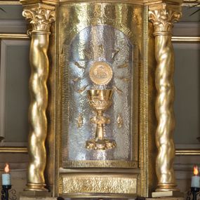 Zdjęcie nr 1: Tabernakulum oparte na schemacie aediculi  na cokole w formie prostopadłościanu. Ścianka frontowa ujęta półfilarami dźwigającymi gzyms opasujący go z trzech stron, na froncie przyjmujący kształt łuku segmentowego, spiętego ustawionymi przeciwstawnie wolutami. Trzony półfilarów dekorowane owocowo-roślinnymi zwisami, pole środkowe skręconymi liśćmi akantu w układzie lustrzanym. Na nim nastawa w formie półokrągłej ścianki dekorowanej płyciną w kształcie stojącego prostokąta zamkniętego łukiem pełnym zdobionym kielichem z unoszącą się ponad nim hostią w otoczeniu promieni. Drzwiczki ujęte skręconymi kolumnami dźwigającymi pełne belkowanie wyłamane na ich osiach i wyniesione w łuk na polem centralnym. Na środku fryzu uskrzydlona główka anielska. Na wyłamanych częściach belkowania wazony płomieniste. Na ściance bocznej tabliczka z inskrypcją „FUNDATORZY / RODZICE I DZIECI I szej KOMUNI ŚW(IĘTEJ) / ROCZNIK 2002 / WYK(ONANE) KRAKÓW / MAJ 2002 R(OKU)”. 