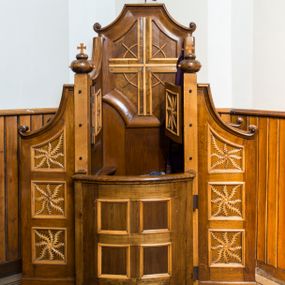 Zdjęcie nr 1: Przyścienny, otwarty konfesjonał szafiasty, wykonany w całości z drewna uzyskał formę architektoniczną ustawioną na niskim cokole. Drewniane siedzisko z podłokietnikami i wysokim zapleckiem flankują dwie ścianki boczne przeprute dwoma kwadratowymi okienkami wypełnionymi romboidalną kratownicą. Ścianki od góry zamknięte są wyciętym, odwróconym łukiem odcinkowym. Od frontu zamykają je smukłe czworoboczne filarki zwieńczone zdwojonymi płaskimi kulami z krzyżykami. W dolnej partii do filarków od przodu przymocowano półwypukłe drzwi. Zdobią je cztery kwadratowe płyciny, obramione profilowanymi listwami. Przestrzeń pomiędzy płycinami tworzy krzyż równoramienny. W górnej części do filarków przymocowano dwuskrzydłowe drzwiczki, których przody ozdobiono płaskorzeźbionym motywem stylizowanego dziewięciosiłu. Podobny motyw wpisano w pola ułożonych w pionowym rzędzie trzech płycin obramionych profilowanymi listwami. Płyciny umieszczono na bocznych policzkach konfesjonału. Górne płyciny uzyskały kształt stojącego trapezu, natomiast pozostałe cztery mają kształt czworoboczny. Policzki wieńczą wolutowe spływy. Zaplecek konfesjonału w górnej części ozdobiony został czworoboczną płyciną o wklęsłych narożach, ujętą szeroką, wklęsło-wypukłą ramą. Pole płyciny ozdobiono krzyżem utworzonym z fazowanych listew, w kształcie zbliżonym do krzyża równoramiennego z wpisanym okręgiem.   