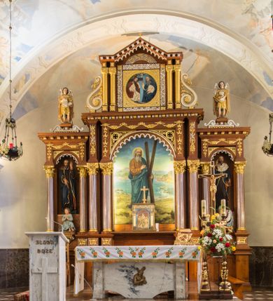 Zdjęcie nr 2: Przyścienną nastawę architektoniczną, trójosiową wykonano z drewna modrzewiowego. Jest to konstrukcja jednokondygnacyjna ze zwieńczeniem, w formie łuku triumfalnego, ustawiona na dwustrefowym cokole. Oś środkową wydzielają dwie pary kolumn o kapitelach kompozytowych i kanelowanych trzonach dźwigających wydłużone imposty. Kolumny wewnętrzne zostały połączone nad polem środkowym fryzem i gzymsem. Z kolei kolumny zewnętrze podtrzymują belkowanie zwieńczenia. Pole środkowe wypełnia nisza w formie stojącego prostokąta zamkniętego łukiem półkolistym z arkaturą z obrazem św. Andrzeja Apostoła. W osiach zewnętrznych usytuowano niższe flankowane parą kanelowanych kolumn z kapitelami kompozytowymi podtrzymujących imposty połączone nad polem fryzem i gzymsem. Nisze uzyskały kształt stojącego prostokąta zamkniętego łukiem półkolistym z arkaturą z figurami św. Wincentego a Paulo i św. Jana Kantego. Ponad niszami na belkowaniu usytuowano cokoły z figurami aniołów trzymających insygnia królewskie. Zwieńczenie uzyskało kształt leżącego prostokąta flankowanego dwiema parami złoconych kolumienek, dźwigających imposty i gzyms nad polem środkowym wyłamanym w trójkąt. Po bokach widoczne są spływy wolutowe. W polu znajduje się rama w formie kwadratu z wpisanym kołem z płaskorzeźbionym przedstawieniem Trójcy Świętej. Cokoły i imposty dekorowane zostały stylizowaną ornamentyką roślinną w postaci zwisów, kampanuli i girland. Struktura nastawy utrzymana jest w kolorze naturalnego drewna, natomiast ornamentyka, detale i profile zostały wyzłocone i wysrebrzone. Z kolei figury i płaskorzeźba w zwieńczeniu uzyskały naturalistyczną polichromię.