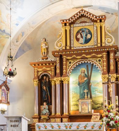 Zdjęcie nr 3: Przyścienną nastawę architektoniczną, trójosiową wykonano z drewna modrzewiowego. Jest to konstrukcja jednokondygnacyjna ze zwieńczeniem, w formie łuku triumfalnego, ustawiona na dwustrefowym cokole. Oś środkową wydzielają dwie pary kolumn o kapitelach kompozytowych i kanelowanych trzonach dźwigających wydłużone imposty. Kolumny wewnętrzne zostały połączone nad polem środkowym fryzem i gzymsem. Z kolei kolumny zewnętrze podtrzymują belkowanie zwieńczenia. Pole środkowe wypełnia nisza w formie stojącego prostokąta zamkniętego łukiem półkolistym z arkaturą z obrazem św. Andrzeja Apostoła. W osiach zewnętrznych usytuowano niższe flankowane parą kanelowanych kolumn z kapitelami kompozytowymi podtrzymujących imposty połączone nad polem fryzem i gzymsem. Nisze uzyskały kształt stojącego prostokąta zamkniętego łukiem półkolistym z arkaturą z figurami św. Wincentego a Paulo i św. Jana Kantego. Ponad niszami na belkowaniu usytuowano cokoły z figurami aniołów trzymających insygnia królewskie. Zwieńczenie uzyskało kształt leżącego prostokąta flankowanego dwiema parami złoconych kolumienek, dźwigających imposty i gzyms nad polem środkowym wyłamanym w trójkąt. Po bokach widoczne są spływy wolutowe. W polu znajduje się rama w formie kwadratu z wpisanym kołem z płaskorzeźbionym przedstawieniem Trójcy Świętej. Cokoły i imposty dekorowane zostały stylizowaną ornamentyką roślinną w postaci zwisów, kampanuli i girland. Struktura nastawy utrzymana jest w kolorze naturalnego drewna, natomiast ornamentyka, detale i profile zostały wyzłocone i wysrebrzone. Z kolei figury i płaskorzeźba w zwieńczeniu uzyskały naturalistyczną polichromię.