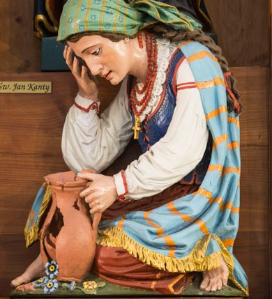 Zdjęcie nr 11: Przyścienną nastawę architektoniczną, trójosiową wykonano z drewna modrzewiowego. Jest to konstrukcja jednokondygnacyjna ze zwieńczeniem, w formie łuku triumfalnego, ustawiona na dwustrefowym cokole. Oś środkową wydzielają dwie pary kolumn o kapitelach kompozytowych i kanelowanych trzonach dźwigających wydłużone imposty. Kolumny wewnętrzne zostały połączone nad polem środkowym fryzem i gzymsem. Z kolei kolumny zewnętrze podtrzymują belkowanie zwieńczenia. Pole środkowe wypełnia nisza w formie stojącego prostokąta zamkniętego łukiem półkolistym z arkaturą z obrazem św. Andrzeja Apostoła. W osiach zewnętrznych usytuowano niższe flankowane parą kanelowanych kolumn z kapitelami kompozytowymi podtrzymujących imposty połączone nad polem fryzem i gzymsem. Nisze uzyskały kształt stojącego prostokąta zamkniętego łukiem półkolistym z arkaturą z figurami św. Wincentego a Paulo i św. Jana Kantego. Ponad niszami na belkowaniu usytuowano cokoły z figurami aniołów trzymających insygnia królewskie. Zwieńczenie uzyskało kształt leżącego prostokąta flankowanego dwiema parami złoconych kolumienek, dźwigających imposty i gzyms nad polem środkowym wyłamanym w trójkąt. Po bokach widoczne są spływy wolutowe. W polu znajduje się rama w formie kwadratu z wpisanym kołem z płaskorzeźbionym przedstawieniem Trójcy Świętej. Cokoły i imposty dekorowane zostały stylizowaną ornamentyką roślinną w postaci zwisów, kampanuli i girland. Struktura nastawy utrzymana jest w kolorze naturalnego drewna, natomiast ornamentyka, detale i profile zostały wyzłocone i wysrebrzone. Z kolei figury i płaskorzeźba w zwieńczeniu uzyskały naturalistyczną polichromię.