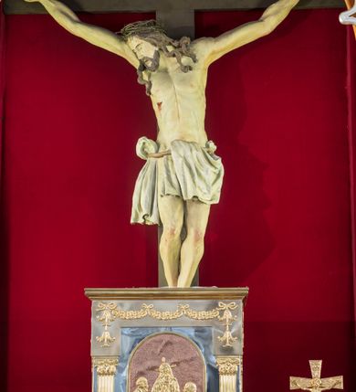 Zdjęcie nr 5: Przyścienną nastawę architektoniczną, trójosiową wykonano z drewna modrzewiowego. Jest to konstrukcja jednokondygnacyjna ze zwieńczeniem, w formie łuku triumfalnego, ustawiona na dwustrefowym cokole. Oś środkową wydzielają dwie pary kolumn o kapitelach kompozytowych i kanelowanych trzonach dźwigających wydłużone imposty. Kolumny wewnętrzne zostały połączone nad polem środkowym fryzem i gzymsem. Z kolei kolumny zewnętrze podtrzymują belkowanie zwieńczenia. Pole środkowe wypełnia nisza w formie stojącego prostokąta zamkniętego łukiem półkolistym z arkaturą z obrazem św. Andrzeja Apostoła. W osiach zewnętrznych usytuowano niższe flankowane parą kanelowanych kolumn z kapitelami kompozytowymi podtrzymujących imposty połączone nad polem fryzem i gzymsem. Nisze uzyskały kształt stojącego prostokąta zamkniętego łukiem półkolistym z arkaturą z figurami św. Wincentego a Paulo i św. Jana Kantego. Ponad niszami na belkowaniu usytuowano cokoły z figurami aniołów trzymających insygnia królewskie. Zwieńczenie uzyskało kształt leżącego prostokąta flankowanego dwiema parami złoconych kolumienek, dźwigających imposty i gzyms nad polem środkowym wyłamanym w trójkąt. Po bokach widoczne są spływy wolutowe. W polu znajduje się rama w formie kwadratu z wpisanym kołem z płaskorzeźbionym przedstawieniem Trójcy Świętej. Cokoły i imposty dekorowane zostały stylizowaną ornamentyką roślinną w postaci zwisów, kampanuli i girland. Struktura nastawy utrzymana jest w kolorze naturalnego drewna, natomiast ornamentyka, detale i profile zostały wyzłocone i wysrebrzone. Z kolei figury i płaskorzeźba w zwieńczeniu uzyskały naturalistyczną polichromię.