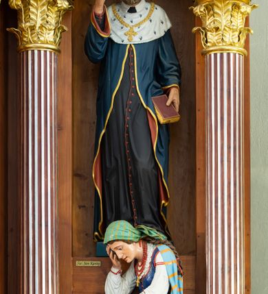 Zdjęcie nr 12: Przyścienną nastawę architektoniczną, trójosiową wykonano z drewna modrzewiowego. Jest to konstrukcja jednokondygnacyjna ze zwieńczeniem, w formie łuku triumfalnego, ustawiona na dwustrefowym cokole. Oś środkową wydzielają dwie pary kolumn o kapitelach kompozytowych i kanelowanych trzonach dźwigających wydłużone imposty. Kolumny wewnętrzne zostały połączone nad polem środkowym fryzem i gzymsem. Z kolei kolumny zewnętrze podtrzymują belkowanie zwieńczenia. Pole środkowe wypełnia nisza w formie stojącego prostokąta zamkniętego łukiem półkolistym z arkaturą z obrazem św. Andrzeja Apostoła. W osiach zewnętrznych usytuowano niższe flankowane parą kanelowanych kolumn z kapitelami kompozytowymi podtrzymujących imposty połączone nad polem fryzem i gzymsem. Nisze uzyskały kształt stojącego prostokąta zamkniętego łukiem półkolistym z arkaturą z figurami św. Wincentego a Paulo i św. Jana Kantego. Ponad niszami na belkowaniu usytuowano cokoły z figurami aniołów trzymających insygnia królewskie. Zwieńczenie uzyskało kształt leżącego prostokąta flankowanego dwiema parami złoconych kolumienek, dźwigających imposty i gzyms nad polem środkowym wyłamanym w trójkąt. Po bokach widoczne są spływy wolutowe. W polu znajduje się rama w formie kwadratu z wpisanym kołem z płaskorzeźbionym przedstawieniem Trójcy Świętej. Cokoły i imposty dekorowane zostały stylizowaną ornamentyką roślinną w postaci zwisów, kampanuli i girland. Struktura nastawy utrzymana jest w kolorze naturalnego drewna, natomiast ornamentyka, detale i profile zostały wyzłocone i wysrebrzone. Z kolei figury i płaskorzeźba w zwieńczeniu uzyskały naturalistyczną polichromię.