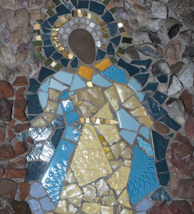 Zdjęcie nr 1: Mozaika w kształcie stojącego prostokąta z umieszczonym centralnie frontalnym przedstawieniem Matki Boskiej w typie Niepokalanie Poczętej. Maria ukazana całopostaciowo, w pozycji stojącej z głową pochyloną nieznacznie w prawo i skierowaną do dołu. Ręce postaci ugięte w łokciach i wyciągnięte na boki. Twarz Marii pozbawiona jest szczegółów fizjonomicznych. Wokół głowy znajduje się nimb w kolorach białym, złotym, ciemnoniebieskim i zielonym. Postać ubrana jest jasnożółtą suknię z długimi rękawami przewiązaną w talii złotym pasem oraz rozwiany płaszcz utrzymany w odcieniach niebieskiego. Spod szat widoczne brązowe buty. Pod stopami postaci widoczny fragment ciemnozielonego owalu nawiązującego do globu, na którym zazwyczaj stoi Maria w przedstawieniach Niepokalanego Poczęcia. Tło jednolite utrzymane w odcieniach brązu i szarości.



