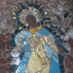 Zdjęcie nr 1: Mozaika w kształcie stojącego prostokąta z umieszczonym centralnie frontalnym przedstawieniem Matki Boskiej w typie Niepokalanie Poczętej. Maria ukazana całopostaciowo, w pozycji stojącej z głową pochyloną nieznacznie w prawo i skierowaną do dołu. Ręce postaci ugięte w łokciach i wyciągnięte na boki. Twarz Marii pozbawiona jest szczegółów fizjonomicznych. Wokół głowy znajduje się nimb w kolorach białym, złotym, ciemnoniebieskim i zielonym. Postać ubrana jest jasnożółtą suknię z długimi rękawami przewiązaną w talii złotym pasem oraz rozwiany płaszcz utrzymany w odcieniach niebieskiego. Spod szat widoczne brązowe buty. Pod stopami postaci widoczny fragment ciemnozielonego owalu nawiązującego do globu, na którym zazwyczaj stoi Maria w przedstawieniach Niepokalanego Poczęcia. Tło jednolite utrzymane w odcieniach brązu i szarości.



