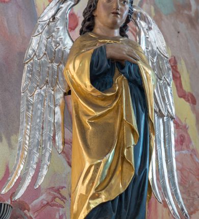 Zdjęcie nr 5: Przyścienną nastawę architektoniczną, trójosiową wykonano z drewna modrzewiowego. Jest to konstrukcja jednokondygnacyjna w formie łuku triumfalnego ze zwieńczeniem, ustawiona na dwustrefowym cokole. Stipes ołtarzowy uzyskał formę leżącego prostopadłościanu flankowanego po bokach spływami wolutowymi. W stipesie od przodu we wnęce pomiędzy dwoma pilastrami podtrzymującymi mensę umieszczono płaskorzeźbę z przedstawieniem Mojżesza wyprowadzającego wodę ze skały. Trzony pilastrów ozdobiono płaskorzeźbionym i złoconym ornamentem roślinnym. Na mensie na osi ustawiono
tabernakulum w formie leżącego prostopadłościanu o ściętych narożach, na niskim cokole, z profilowanym, niewielkim gzymsem, flankowanym na narożach pilastrami. Ścianka frontowa obwiedziona została rzędem złoconych okręgów. Na drzwiczkach umieszczono symbol Opatrzności Bożej od góry ujęte półkolistym łukiem. Oś środkową nastawy wydzielają dwie kolumny o kapitelach kompozytowych i kanelowanych trzonach dźwigających wydłużone imposty. Kolumny zostały połączone nad polem środkowym fryzem i gzymsem. Pole środkowe wypełnia nisza w formie stojącego prostokąta zamkniętego łukiem półkolistym z arkaturą z figurą św. Antoniego  Padwy oraz dwoma obrazami na zasuwach - "Niewiasty idące z Golgoty" oraz "Miłosierdzie Boże". W osiach zewnętrznych usytuowano niższe flankowane kanelowanymi kolumnami z kapitelami kompozytowymi, podtrzymującymi imposty połączone nad polem fryzem i gzymsem. Nisze uzyskały kształt stojącego prostokąta zamkniętego łukiem półkolistym z arkaturą z figurami apostołów św. Piotra i św. Pawła. Ponad niszami na belkowaniu usytuowano cokoły z figurami stojących aniołów ze złożonymi do modlitwy rękami. Zwieńczenie uzyskało kształt stojącego prostokąta flankowanego dwiema parami złoconych kolumienek, dźwigających imposty i gzyms nad polem środkowym wyłamanym w trójkąt. Po bokach widoczne są spływy wolutowe. Gzyms wieńczy krzyż i dwie złocone wazy. W polu zwieńczenia znajduje się rama w formie prostokąta z wpisanym owalem z obrazem św. Siostry Faustyny Kowalskiej. Ponad ramą widoczny jest chrystogram "IHS". Cokoły i imposty dekorowane zostały stylizowaną ornamentyką roślinną w postaci zwisów, kampanuli i girland. Struktura nastawy utrzymana jest w kolorze naturalnego drewna, natomiast ornamentyka, detale i profile zostały wyzłocone i wysrebrzone. Z kolei figury uzyskały naturalistyczną polichromię.