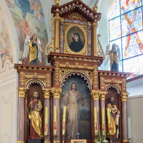 Zdjęcie nr 1: Przyścienną nastawę architektoniczną, trójosiową wykonano z drewna modrzewiowego. Jest to konstrukcja jednokondygnacyjna w formie łuku triumfalnego ze zwieńczeniem, ustawiona na dwustrefowym cokole. Stipes ołtarzowy uzyskał formę leżącego prostopadłościanu flankowanego po bokach spływami wolutowymi. W stipesie od przodu we wnęce pomiędzy dwoma pilastrami podtrzymującymi mensę umieszczono płaskorzeźbę z przedstawieniem Mojżesza wyprowadzającego wodę ze skały. Trzony pilastrów ozdobiono płaskorzeźbionym i złoconym ornamentem roślinnym. Na mensie na osi ustawiono
tabernakulum w formie leżącego prostopadłościanu o ściętych narożach, na niskim cokole, z profilowanym, niewielkim gzymsem, flankowanym na narożach pilastrami. Ścianka frontowa obwiedziona została rzędem złoconych okręgów. Na drzwiczkach umieszczono symbol Opatrzności Bożej od góry ujęte półkolistym łukiem. Oś środkową nastawy wydzielają dwie kolumny o kapitelach kompozytowych i kanelowanych trzonach dźwigających wydłużone imposty. Kolumny zostały połączone nad polem środkowym fryzem i gzymsem. Pole środkowe wypełnia nisza w formie stojącego prostokąta zamkniętego łukiem półkolistym z arkaturą z figurą św. Antoniego  Padwy oraz dwoma obrazami na zasuwach - "Niewiasty idące z Golgoty" oraz "Miłosierdzie Boże". W osiach zewnętrznych usytuowano niższe flankowane kanelowanymi kolumnami z kapitelami kompozytowymi, podtrzymującymi imposty połączone nad polem fryzem i gzymsem. Nisze uzyskały kształt stojącego prostokąta zamkniętego łukiem półkolistym z arkaturą z figurami apostołów św. Piotra i św. Pawła. Ponad niszami na belkowaniu usytuowano cokoły z figurami stojących aniołów ze złożonymi do modlitwy rękami. Zwieńczenie uzyskało kształt stojącego prostokąta flankowanego dwiema parami złoconych kolumienek, dźwigających imposty i gzyms nad polem środkowym wyłamanym w trójkąt. Po bokach widoczne są spływy wolutowe. Gzyms wieńczy krzyż i dwie złocone wazy. W polu zwieńczenia znajduje się rama w formie prostokąta z wpisanym owalem z obrazem św. Siostry Faustyny Kowalskiej. Ponad ramą widoczny jest chrystogram "IHS". Cokoły i imposty dekorowane zostały stylizowaną ornamentyką roślinną w postaci zwisów, kampanuli i girland. Struktura nastawy utrzymana jest w kolorze naturalnego drewna, natomiast ornamentyka, detale i profile zostały wyzłocone i wysrebrzone. Z kolei figury uzyskały naturalistyczną polichromię.