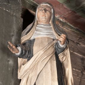 Zdjęcie nr 1: Rzeźba pełnoplastyczna, przyścienna, ścięta z tyłu, przedstawiająca świętą zakonnicę, być może dominikankę (?), umieszczona po prawej stronie glorii w zwieńczeniu ołtarza bocznego. Postać ukazana frontalnie, w pozycji stojącej, z ugiętą w kolanie prawą nogą, ręce zgięte w łokciach, wysunięte do przodu. W prawej dłoni święta trzyma otwartą księgę. Święta ubrana w czarny habit z białym szkaplerzem i biały płaszcz, którego prawa poła przełożona ukośnie przez przód postaci; na głowie czarny welon, wokół twarzy podwika. Twarz pociągła z wydatnym nosem, oczy o opadających zewnętrznych kącikach, usta lekko rozchylone.
