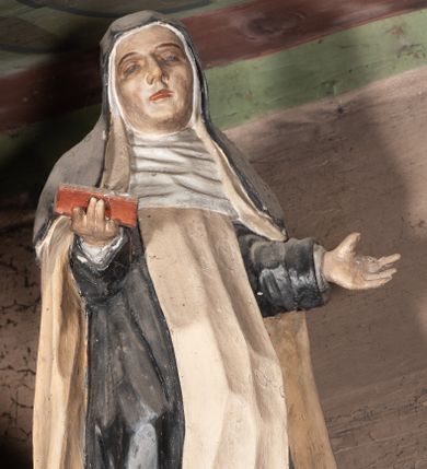 Zdjęcie nr 1: Rzeźba pełnoplastyczna, przyścienna, ścięta z tyłu, przedstawiająca świętą zakonnicę, być może dominikankę (?), umieszczona po lewej stronie glorii w zwieńczeniu ołtarza bocznego. Postać ukazana frontalnie, w pozycji stojącej, z ugiętą w kolanie prawą nogą, ręce zgięte w łokciach, wysunięte do przodu. Święta ubrana w czarny habit z białym szkaplerzem i biały płaszcz; na głowie czarny welon, wokół twarzy podwika. Twarz pociągła z wydatnym nosem, oczy o opadających zewnętrznych kącikach, usta lekko rozchylone.