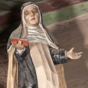 Zdjęcie nr 1: Rzeźba pełnoplastyczna, przyścienna, ścięta z tyłu, przedstawiająca świętą zakonnicę, być może dominikankę (?), umieszczona po lewej stronie glorii w zwieńczeniu ołtarza bocznego. Postać ukazana frontalnie, w pozycji stojącej, z ugiętą w kolanie prawą nogą, ręce zgięte w łokciach, wysunięte do przodu. Święta ubrana w czarny habit z białym szkaplerzem i biały płaszcz; na głowie czarny welon, wokół twarzy podwika. Twarz pociągła z wydatnym nosem, oczy o opadających zewnętrznych kącikach, usta lekko rozchylone.