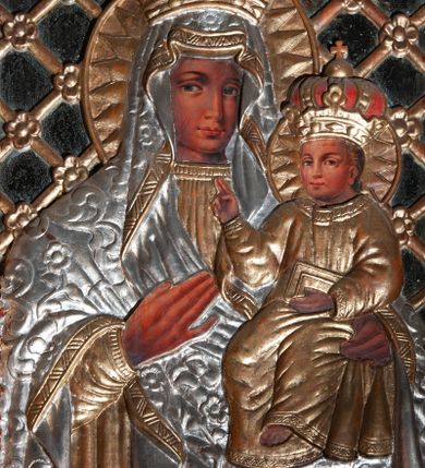 Zdjęcie nr 1: Obraz w kształcie stojącego prostokąta; ujęty drewnianą ramą, dekorowaną płaskorzeźbionym motywem liści akantu; przedstawienie Matki Boskiej z Dzieciątkiem w typie Matki Boskiej Bocheńskiej. Pośrodku drewniana, płaskorzeźbiona półpostać Matki Boskiej, lekko zwróconej w lewo. Na lewym ramieniu podtrzymuje Dzieciątko, prawą dłonią wskazuje na nie. Twarz i dłonie malowane olejno na desce. Twarz owalna, o ciemnej karnacji, rysach wydobytych światłocieniem; oczy duże, w kształcie migdału; nos duży, długi, prosty; usta niewielkie, pełne. Ubrana w płaskorzeźbioną, złotą suknię, z długim, wąskim rękawem; drapowaną w równoległe, rurkowate fałdy oraz srebrzony maforion o wzorze roślinnym, ze złoconą lamówką, narzucony na głowę i ramiona, otaczający ściśle postać oraz opadający diagonalnie, delikatnymi rurkowatymi fałdami. Dzieciątko siedzi na ramieniu Matki, zwrócone en trois quarts w prawo. Lewą ręką przytrzymuje na kolanach księgę; prawą unosi w geście błogosławieństwa. Twarz i dłonie malowane olejno na desce. Twarz okrągła, o pełnych policzkach i ciemnej karnacji; oczy niewielkie, prosty nos i pełne usta. Włosy krótkie, jasne. Ubrane w długą, złoconą, delikatnie drapowaną szatę, z długimi, wąskimi rękawami, z dekoracyjną lamówką przy szyi. Wokół głowy obu postaci płaskorzeźbione zamknięte nimby promieniste oraz zamknięte korony. Tło lustrzane wypełnione ukośną, złoconą kratką z rozetkami na przecięciach listew. Kolorystyka ciepła, brunatna, bryła wydobyta światłocieniem, delikatne przejścia tonalne.