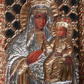 Zdjęcie nr 1: Obraz w kształcie stojącego prostokąta; ujęty drewnianą ramą, dekorowaną płaskorzeźbionym motywem liści akantu; przedstawienie Matki Boskiej z Dzieciątkiem w typie Matki Boskiej Bocheńskiej. Pośrodku drewniana, płaskorzeźbiona półpostać Matki Boskiej, lekko zwróconej w lewo. Na lewym ramieniu podtrzymuje Dzieciątko, prawą dłonią wskazuje na nie. Twarz i dłonie malowane olejno na desce. Twarz owalna, o ciemnej karnacji, rysach wydobytych światłocieniem; oczy duże, w kształcie migdału; nos duży, długi, prosty; usta niewielkie, pełne. Ubrana w płaskorzeźbioną, złotą suknię, z długim, wąskim rękawem; drapowaną w równoległe, rurkowate fałdy oraz srebrzony maforion o wzorze roślinnym, ze złoconą lamówką, narzucony na głowę i ramiona, otaczający ściśle postać oraz opadający diagonalnie, delikatnymi rurkowatymi fałdami. Dzieciątko siedzi na ramieniu Matki, zwrócone en trois quarts w prawo. Lewą ręką przytrzymuje na kolanach księgę; prawą unosi w geście błogosławieństwa. Twarz i dłonie malowane olejno na desce. Twarz okrągła, o pełnych policzkach i ciemnej karnacji; oczy niewielkie, prosty nos i pełne usta. Włosy krótkie, jasne. Ubrane w długą, złoconą, delikatnie drapowaną szatę, z długimi, wąskimi rękawami, z dekoracyjną lamówką przy szyi. Wokół głowy obu postaci płaskorzeźbione zamknięte nimby promieniste oraz zamknięte korony. Tło lustrzane wypełnione ukośną, złoconą kratką z rozetkami na przecięciach listew. Kolorystyka ciepła, brunatna, bryła wydobyta światłocieniem, delikatne przejścia tonalne.