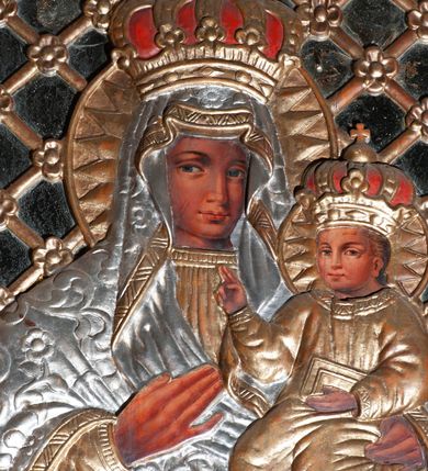 Zdjęcie nr 2: Obraz w kształcie stojącego prostokąta; ujęty drewnianą ramą, dekorowaną płaskorzeźbionym motywem liści akantu; przedstawienie Matki Boskiej z Dzieciątkiem w typie Matki Boskiej Bocheńskiej. Pośrodku drewniana, płaskorzeźbiona półpostać Matki Boskiej, lekko zwróconej w lewo. Na lewym ramieniu podtrzymuje Dzieciątko, prawą dłonią wskazuje na nie. Twarz i dłonie malowane olejno na desce. Twarz owalna, o ciemnej karnacji, rysach wydobytych światłocieniem; oczy duże, w kształcie migdału; nos duży, długi, prosty; usta niewielkie, pełne. Ubrana w płaskorzeźbioną, złotą suknię, z długim, wąskim rękawem; drapowaną w równoległe, rurkowate fałdy oraz srebrzony maforion o wzorze roślinnym, ze złoconą lamówką, narzucony na głowę i ramiona, otaczający ściśle postać oraz opadający diagonalnie, delikatnymi rurkowatymi fałdami. Dzieciątko siedzi na ramieniu Matki, zwrócone en trois quarts w prawo. Lewą ręką przytrzymuje na kolanach księgę; prawą unosi w geście błogosławieństwa. Twarz i dłonie malowane olejno na desce. Twarz okrągła, o pełnych policzkach i ciemnej karnacji; oczy niewielkie, prosty nos i pełne usta. Włosy krótkie, jasne. Ubrane w długą, złoconą, delikatnie drapowaną szatę, z długimi, wąskimi rękawami, z dekoracyjną lamówką przy szyi. Wokół głowy obu postaci płaskorzeźbione zamknięte nimby promieniste oraz zamknięte korony. Tło lustrzane wypełnione ukośną, złoconą kratką z rozetkami na przecięciach listew. Kolorystyka ciepła, brunatna, bryła wydobyta światłocieniem, delikatne przejścia tonalne.