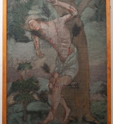 Zdjęcie nr 2: Obraz w kształcie stojącego prostokąta, malowany olejno na desce, w wąskiej drewnianej ramce, z przedstawieniem męczeństwa św. Sebastiana. Święty przedstawiony w całej postaci, zwrócony w prawo, stoi przywiązany do drzewa, oparty biodrami o pień, ze skrzyżowanymi nogami i z rękami wzniesionymi do góry. Ciało nagie, muskularne, o zaburzonych proporcjach; wokół bioder biała draperia przewiązana z przodu. W ciało wbite kilka dużych strzał. Po prawej stronie w głębi duża postać ludzka o ciemnych zwichrzonych włosach. W tle zarys pejzażu.