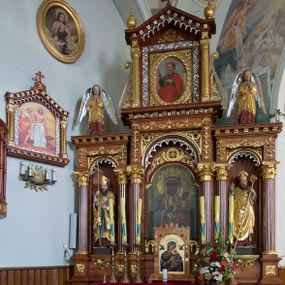 Zdjęcie nr 1: Przyścienną nastawę architektoniczną, trójosiową wykonano z drewna modrzewiowego. Jest to konstrukcja jednokondygnacyjna w formie łuku triumfalnego ze zwieńczeniem, ustawiona na dwustrefowym cokole. Stipes ołtarzowy uzyskał formę leżącego prostopadłościanu flankowanego po bokach spływami wolutowymi. W stipesie od przodu we wnęce pomiędzy dwoma pilastrami podtrzymującymi mensę umieszczono płaskorzeźbę z przedstawieniem odnoszącym się najprawdopodobniej do życia proroka Jonasza. Trzony pilastrów ozdobiono płaskorzeźbionym i złoconym ornamentem roślinnym. Oś środkową nastawy wydzielają dwie kolumny o kapitelach korynckich i kanelowanych trzonach dźwigających wydłużone imposty. Kolumny zostały połączone nad polem środkowym fryzem i gzymsem. Pole środkowe wypełnia nisza w formie stojącego prostokąta zamkniętego łukiem półkolistym z arkaturą z półkoliście zamkniętym obrazem Matki Boskiej Częstochowskiej. Na zasuwie umieszczono obraz św. Franciszka z Asyżu. W osiach zewnętrznych usytuowano niższe flankowane kanelowanymi kolumnami z kapitelami kompozytowymi, podtrzymującymi imposty połączone nad polem fryzem i gzymsem. Nisze uzyskały kształt stojącego prostokąta zamkniętego łukiem półkolistym z arkaturą z figurami św. Wojciecha i św. Stanisława. Ponad niszami na belkowaniu usytuowano cokoły z figurami stojących aniołów ze złożonymi do modlitwy rękami. Zwieńczenie uzyskało kształt stojącego prostokąta flankowanego dwiema parami złoconych kolumienek, dźwigających imposty i gzyms nad polem środkowym wyłamanym w trójkąt. Po bokach widoczne są spływy wolutowe. Gzyms wieńczy krzyż i dwie złocone wazy. W polu zwieńczenia znajduje się rama w formie prostokąta z wpisanym owalem z obrazem św. Bartłomieja Apostoła. Ponad ramą widoczny jest monogram maryjny. Cokoły i imposty dekorowane zostały stylizowaną ornamentyką roślinną w postaci zwisów, kampanuli i girland. Struktura nastawy utrzymana jest w kolorze naturalnego drewna, natomiast ornamentyka, detale i profile zostały wyzłocone i wysrebrzone. Z kolei figury uzyskały naturalistyczną polichromię.