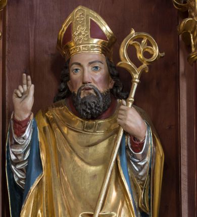 Zdjęcie nr 1: Rzeźba z przedstawieniem św. Stanisława, biskupa jest drążona od tyłu. Biskup został ustawiony na prostopadłościennym postumencie. Świętego przedstawiono frontalnie w całej postaci w nieznacznym kontrapoście. Prawą rękę ma uniesioną w geście błogosławieństwa, zaś w lewej trzyma pastorał o krzywaśni utworzonej ze stylizowanej wici roślinnej. Męczennika ukazano jako dojrzałego mężczyznę z pociągłą twarzą, długimi, ciemnymi, falowanymi włosami spływającymi na ramiona oraz brodą. Ma prosty nos oraz wydatne usta i szeroko otwarte oczy o spojrzeniu skierowanym przed siebie. Ubrany jest w długą czerwoną albę, srebrną dalmatykę z długimi rękawami, zdobioną u dołu geometryczną ornamentyką, spod której widać końce złotej stuły. Na wierzchu biskup ma złoty ornat o kolistym wykroju z błękitnawą podszewką. Na jego głowie widoczna jest czerwono-złota infuła. Pod lewą, obutą stopą leży złamany srebrzony miecz. Do postumentu przymocowano tabliczkę z napisem: "Ofiarę na renowację ołtarza złożyli Czesław Tomala i Katarzyna żona z d(omu) Benedyków; Jan Grele i Zofia żona z d(omu) Benedyków. Bóg zapłać". 