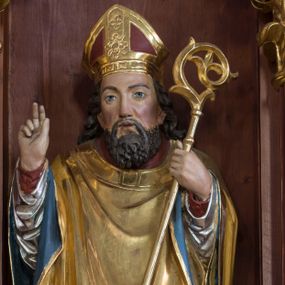 Zdjęcie nr 1: Rzeźba z przedstawieniem św. Stanisława, biskupa jest drążona od tyłu. Biskup został ustawiony na prostopadłościennym postumencie. Świętego przedstawiono frontalnie w całej postaci w nieznacznym kontrapoście. Prawą rękę ma uniesioną w geście błogosławieństwa, zaś w lewej trzyma pastorał o krzywaśni utworzonej ze stylizowanej wici roślinnej. Męczennika ukazano jako dojrzałego mężczyznę z pociągłą twarzą, długimi, ciemnymi, falowanymi włosami spływającymi na ramiona oraz brodą. Ma prosty nos oraz wydatne usta i szeroko otwarte oczy o spojrzeniu skierowanym przed siebie. Ubrany jest w długą czerwoną albę, srebrną dalmatykę z długimi rękawami, zdobioną u dołu geometryczną ornamentyką, spod której widać końce złotej stuły. Na wierzchu biskup ma złoty ornat o kolistym wykroju z błękitnawą podszewką. Na jego głowie widoczna jest czerwono-złota infuła. Pod lewą, obutą stopą leży złamany srebrzony miecz. Do postumentu przymocowano tabliczkę z napisem: "Ofiarę na renowację ołtarza złożyli Czesław Tomala i Katarzyna żona z d(omu) Benedyków; Jan Grele i Zofia żona z d(omu) Benedyków. Bóg zapłać". 