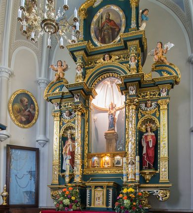 Zdjęcie nr 3: Ołtarz w kaplicy Matki Boskiej Szaflarskiej stanowi przykład przyściennej, architektonicznej, drewnianej nastawy trójosiowej ze zwieńczeniem. Stipes ołtarzowy z drewnianą mensą z kamiennym portatylem uzyskał kształt leżącego prostopadłościanu. Jego przód flankują hermy o trzonach dekorowanych cekinami. W polu zastosowano prostokątną płycinę ujętą kimationem. Na mensie ustawiono prostopadłościenne tabernakulum z wyodrębnionym cokołem i gzymsem koronującym wyłamanym na osi, podtrzymywanym przez dwa pilastry. Krawędzie tabernakulum zdobi imitacja boniowania. Drzwiczki ozdobiono stojącą, prostokątną płyciną, zwieńczoną trójkątnym przyczółkiem. W polu płyciny umieszczono stojący na obłokach płaskorzeźbiony i złocony kielich z hostią otoczoną promieniami. Jednokondygnacyjna nastawa wspiera się na prostokątnej predelli, przechodzącej pod osiami bocznymi w wolutowe konsole. Osie retabulum wydzielone zostały za pomocą skrajnych pilastrów oraz pary kolumn flankujących oś środkową. Podpory dźwigają pełne belkowanie wyłamane na ich osi, przerwane w partii pola środkowego oraz na osiach skrajnych przerwany półokrągły przyczółek. Wewnętrzna para kolumn dźwiga dodatkowo parę konsol podtrzymujących pełne belkowanie wyłamane na ich osi. Zwieńczenie uzyskało formę kwadratu zamkniętego szczytem z krzyżem, ujętego parą kolumienek na cokołach podtrzymujących skrajne woluty. Po zewnętrznych bokach zwieńczenia usytuowano postacie adorujących aniołów. W polu środkowym kondygnacji znalazła się nisza w formie stojącego prostokąta zamkniętego archiwoltą opadającą na belkowanie z konchą wydzieloną przez poziomy gzyms wsparty na dwóch pilastrach. W podniebiu konchy widoczna jest rzeźbiona i srebrzona gołębica Ducha Świętego. W niszy ustawiono figurę Matki Boskiej z Dzieciątkiem stojącą na wysokim czworobocznym postumencie. W osiach bocznych znalazły się nisze zamknięte konchą, u dołu podtrzymywane wspornikiem, z figurami św. Elżbiety Węgierskiej i św. Kazimierza Królewicza. W polu zwieńczenia umieszczono obraz w formie owalu ujęty ramą z przedstawieniem św. Maurycego. Ołtarz w całości pokryty został bogatą i zróżnicowaną dekoracją ornamentalną. Liśćmi akantu ozdobiono cokoły kolumn i wolut podwieszonych pod boczne osie. Kolumny w jednej czwartej wysokości obwiedzione zostały profilowaną listwą wypełnioną rautami. Ich dolne części ozdobiono uskrzydlonymi główkami aniołów z podwieszonymi festonami i girlandami. Z kolei w górnych partiach wykorzystano spiralne wici winnego grona. Dekoracyjnie artykułowano także pilastry, które w jednej czwartej przedzielono profilowanym gzymsem. Ich dolne części szczelnie wypełniono ornamentem okuciowym z rautem w środku, z kolei górne pokryto układającą się swobodnie i symetrycznie wstęgą z kaboszonami. Fryz belkowania wypełniony został wicią roślinną. Pola pomiędzy niszą a belkowaniem ozdobiono uskrzydlonymi główkami aniołów i podwieszonymi pod nimi girlandami. Ponadto uskrzydlone główki aniołów zdobią imposty podstawy zwieńczenia oraz klucz archiwolty ponad niszą główną. Kolumieńki zwieńczenia ozdobione zostały układającą się spiralnie wstęgą. Na dekoracje ornamentalną nastawy składają się również różne zdobienia profilów belkowania i zwieńczenia w postaci kostkowania, wolich oczu oraz pasów utworzonych z liści akantu.
