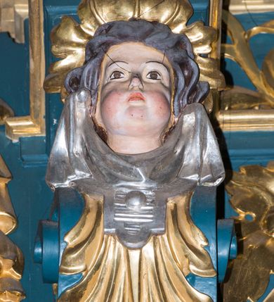 Zdjęcie nr 12: Ołtarz w kaplicy Matki Boskiej Szaflarskiej stanowi przykład przyściennej, architektonicznej, drewnianej nastawy trójosiowej ze zwieńczeniem. Stipes ołtarzowy z drewnianą mensą z kamiennym portatylem uzyskał kształt leżącego prostopadłościanu. Jego przód flankują hermy o trzonach dekorowanych cekinami. W polu zastosowano prostokątną płycinę ujętą kimationem. Na mensie ustawiono prostopadłościenne tabernakulum z wyodrębnionym cokołem i gzymsem koronującym wyłamanym na osi, podtrzymywanym przez dwa pilastry. Krawędzie tabernakulum zdobi imitacja boniowania. Drzwiczki ozdobiono stojącą, prostokątną płyciną, zwieńczoną trójkątnym przyczółkiem. W polu płyciny umieszczono stojący na obłokach płaskorzeźbiony i złocony kielich z hostią otoczoną promieniami. Jednokondygnacyjna nastawa wspiera się na prostokątnej predelli, przechodzącej pod osiami bocznymi w wolutowe konsole. Osie retabulum wydzielone zostały za pomocą skrajnych pilastrów oraz pary kolumn flankujących oś środkową. Podpory dźwigają pełne belkowanie wyłamane na ich osi, przerwane w partii pola środkowego oraz na osiach skrajnych przerwany półokrągły przyczółek. Wewnętrzna para kolumn dźwiga dodatkowo parę konsol podtrzymujących pełne belkowanie wyłamane na ich osi. Zwieńczenie uzyskało formę kwadratu zamkniętego szczytem z krzyżem, ujętego parą kolumienek na cokołach podtrzymujących skrajne woluty. Po zewnętrznych bokach zwieńczenia usytuowano postacie adorujących aniołów. W polu środkowym kondygnacji znalazła się nisza w formie stojącego prostokąta zamkniętego archiwoltą opadającą na belkowanie z konchą wydzieloną przez poziomy gzyms wsparty na dwóch pilastrach. W podniebiu konchy widoczna jest rzeźbiona i srebrzona gołębica Ducha Świętego. W niszy ustawiono figurę Matki Boskiej z Dzieciątkiem stojącą na wysokim czworobocznym postumencie. W osiach bocznych znalazły się nisze zamknięte konchą, u dołu podtrzymywane wspornikiem, z figurami św. Elżbiety Węgierskiej i św. Kazimierza Królewicza. W polu zwieńczenia umieszczono obraz w formie owalu ujęty ramą z przedstawieniem św. Maurycego. Ołtarz w całości pokryty został bogatą i zróżnicowaną dekoracją ornamentalną. Liśćmi akantu ozdobiono cokoły kolumn i wolut podwieszonych pod boczne osie. Kolumny w jednej czwartej wysokości obwiedzione zostały profilowaną listwą wypełnioną rautami. Ich dolne części ozdobiono uskrzydlonymi główkami aniołów z podwieszonymi festonami i girlandami. Z kolei w górnych partiach wykorzystano spiralne wici winnego grona. Dekoracyjnie artykułowano także pilastry, które w jednej czwartej przedzielono profilowanym gzymsem. Ich dolne części szczelnie wypełniono ornamentem okuciowym z rautem w środku, z kolei górne pokryto układającą się swobodnie i symetrycznie wstęgą z kaboszonami. Fryz belkowania wypełniony został wicią roślinną. Pola pomiędzy niszą a belkowaniem ozdobiono uskrzydlonymi główkami aniołów i podwieszonymi pod nimi girlandami. Ponadto uskrzydlone główki aniołów zdobią imposty podstawy zwieńczenia oraz klucz archiwolty ponad niszą główną. Kolumieńki zwieńczenia ozdobione zostały układającą się spiralnie wstęgą. Na dekoracje ornamentalną nastawy składają się również różne zdobienia profilów belkowania i zwieńczenia w postaci kostkowania, wolich oczu oraz pasów utworzonych z liści akantu.
