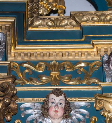 Zdjęcie nr 16: Ołtarz w kaplicy Matki Boskiej Szaflarskiej stanowi przykład przyściennej, architektonicznej, drewnianej nastawy trójosiowej ze zwieńczeniem. Stipes ołtarzowy z drewnianą mensą z kamiennym portatylem uzyskał kształt leżącego prostopadłościanu. Jego przód flankują hermy o trzonach dekorowanych cekinami. W polu zastosowano prostokątną płycinę ujętą kimationem. Na mensie ustawiono prostopadłościenne tabernakulum z wyodrębnionym cokołem i gzymsem koronującym wyłamanym na osi, podtrzymywanym przez dwa pilastry. Krawędzie tabernakulum zdobi imitacja boniowania. Drzwiczki ozdobiono stojącą, prostokątną płyciną, zwieńczoną trójkątnym przyczółkiem. W polu płyciny umieszczono stojący na obłokach płaskorzeźbiony i złocony kielich z hostią otoczoną promieniami. Jednokondygnacyjna nastawa wspiera się na prostokątnej predelli, przechodzącej pod osiami bocznymi w wolutowe konsole. Osie retabulum wydzielone zostały za pomocą skrajnych pilastrów oraz pary kolumn flankujących oś środkową. Podpory dźwigają pełne belkowanie wyłamane na ich osi, przerwane w partii pola środkowego oraz na osiach skrajnych przerwany półokrągły przyczółek. Wewnętrzna para kolumn dźwiga dodatkowo parę konsol podtrzymujących pełne belkowanie wyłamane na ich osi. Zwieńczenie uzyskało formę kwadratu zamkniętego szczytem z krzyżem, ujętego parą kolumienek na cokołach podtrzymujących skrajne woluty. Po zewnętrznych bokach zwieńczenia usytuowano postacie adorujących aniołów. W polu środkowym kondygnacji znalazła się nisza w formie stojącego prostokąta zamkniętego archiwoltą opadającą na belkowanie z konchą wydzieloną przez poziomy gzyms wsparty na dwóch pilastrach. W podniebiu konchy widoczna jest rzeźbiona i srebrzona gołębica Ducha Świętego. W niszy ustawiono figurę Matki Boskiej z Dzieciątkiem stojącą na wysokim czworobocznym postumencie. W osiach bocznych znalazły się nisze zamknięte konchą, u dołu podtrzymywane wspornikiem, z figurami św. Elżbiety Węgierskiej i św. Kazimierza Królewicza. W polu zwieńczenia umieszczono obraz w formie owalu ujęty ramą z przedstawieniem św. Maurycego. Ołtarz w całości pokryty został bogatą i zróżnicowaną dekoracją ornamentalną. Liśćmi akantu ozdobiono cokoły kolumn i wolut podwieszonych pod boczne osie. Kolumny w jednej czwartej wysokości obwiedzione zostały profilowaną listwą wypełnioną rautami. Ich dolne części ozdobiono uskrzydlonymi główkami aniołów z podwieszonymi festonami i girlandami. Z kolei w górnych partiach wykorzystano spiralne wici winnego grona. Dekoracyjnie artykułowano także pilastry, które w jednej czwartej przedzielono profilowanym gzymsem. Ich dolne części szczelnie wypełniono ornamentem okuciowym z rautem w środku, z kolei górne pokryto układającą się swobodnie i symetrycznie wstęgą z kaboszonami. Fryz belkowania wypełniony został wicią roślinną. Pola pomiędzy niszą a belkowaniem ozdobiono uskrzydlonymi główkami aniołów i podwieszonymi pod nimi girlandami. Ponadto uskrzydlone główki aniołów zdobią imposty podstawy zwieńczenia oraz klucz archiwolty ponad niszą główną. Kolumieńki zwieńczenia ozdobione zostały układającą się spiralnie wstęgą. Na dekoracje ornamentalną nastawy składają się również różne zdobienia profilów belkowania i zwieńczenia w postaci kostkowania, wolich oczu oraz pasów utworzonych z liści akantu.
