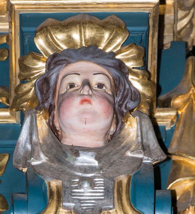 Zdjęcie nr 13: Ołtarz w kaplicy Matki Boskiej Szaflarskiej stanowi przykład przyściennej, architektonicznej, drewnianej nastawy trójosiowej ze zwieńczeniem. Stipes ołtarzowy z drewnianą mensą z kamiennym portatylem uzyskał kształt leżącego prostopadłościanu. Jego przód flankują hermy o trzonach dekorowanych cekinami. W polu zastosowano prostokątną płycinę ujętą kimationem. Na mensie ustawiono prostopadłościenne tabernakulum z wyodrębnionym cokołem i gzymsem koronującym wyłamanym na osi, podtrzymywanym przez dwa pilastry. Krawędzie tabernakulum zdobi imitacja boniowania. Drzwiczki ozdobiono stojącą, prostokątną płyciną, zwieńczoną trójkątnym przyczółkiem. W polu płyciny umieszczono stojący na obłokach płaskorzeźbiony i złocony kielich z hostią otoczoną promieniami. Jednokondygnacyjna nastawa wspiera się na prostokątnej predelli, przechodzącej pod osiami bocznymi w wolutowe konsole. Osie retabulum wydzielone zostały za pomocą skrajnych pilastrów oraz pary kolumn flankujących oś środkową. Podpory dźwigają pełne belkowanie wyłamane na ich osi, przerwane w partii pola środkowego oraz na osiach skrajnych przerwany półokrągły przyczółek. Wewnętrzna para kolumn dźwiga dodatkowo parę konsol podtrzymujących pełne belkowanie wyłamane na ich osi. Zwieńczenie uzyskało formę kwadratu zamkniętego szczytem z krzyżem, ujętego parą kolumienek na cokołach podtrzymujących skrajne woluty. Po zewnętrznych bokach zwieńczenia usytuowano postacie adorujących aniołów. W polu środkowym kondygnacji znalazła się nisza w formie stojącego prostokąta zamkniętego archiwoltą opadającą na belkowanie z konchą wydzieloną przez poziomy gzyms wsparty na dwóch pilastrach. W podniebiu konchy widoczna jest rzeźbiona i srebrzona gołębica Ducha Świętego. W niszy ustawiono figurę Matki Boskiej z Dzieciątkiem stojącą na wysokim czworobocznym postumencie. W osiach bocznych znalazły się nisze zamknięte konchą, u dołu podtrzymywane wspornikiem, z figurami św. Elżbiety Węgierskiej i św. Kazimierza Królewicza. W polu zwieńczenia umieszczono obraz w formie owalu ujęty ramą z przedstawieniem św. Maurycego. Ołtarz w całości pokryty został bogatą i zróżnicowaną dekoracją ornamentalną. Liśćmi akantu ozdobiono cokoły kolumn i wolut podwieszonych pod boczne osie. Kolumny w jednej czwartej wysokości obwiedzione zostały profilowaną listwą wypełnioną rautami. Ich dolne części ozdobiono uskrzydlonymi główkami aniołów z podwieszonymi festonami i girlandami. Z kolei w górnych partiach wykorzystano spiralne wici winnego grona. Dekoracyjnie artykułowano także pilastry, które w jednej czwartej przedzielono profilowanym gzymsem. Ich dolne części szczelnie wypełniono ornamentem okuciowym z rautem w środku, z kolei górne pokryto układającą się swobodnie i symetrycznie wstęgą z kaboszonami. Fryz belkowania wypełniony został wicią roślinną. Pola pomiędzy niszą a belkowaniem ozdobiono uskrzydlonymi główkami aniołów i podwieszonymi pod nimi girlandami. Ponadto uskrzydlone główki aniołów zdobią imposty podstawy zwieńczenia oraz klucz archiwolty ponad niszą główną. Kolumieńki zwieńczenia ozdobione zostały układającą się spiralnie wstęgą. Na dekoracje ornamentalną nastawy składają się również różne zdobienia profilów belkowania i zwieńczenia w postaci kostkowania, wolich oczu oraz pasów utworzonych z liści akantu.
