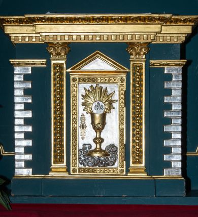 Zdjęcie nr 21: Ołtarz w kaplicy Matki Boskiej Szaflarskiej stanowi przykład przyściennej, architektonicznej, drewnianej nastawy trójosiowej ze zwieńczeniem. Stipes ołtarzowy z drewnianą mensą z kamiennym portatylem uzyskał kształt leżącego prostopadłościanu. Jego przód flankują hermy o trzonach dekorowanych cekinami. W polu zastosowano prostokątną płycinę ujętą kimationem. Na mensie ustawiono prostopadłościenne tabernakulum z wyodrębnionym cokołem i gzymsem koronującym wyłamanym na osi, podtrzymywanym przez dwa pilastry. Krawędzie tabernakulum zdobi imitacja boniowania. Drzwiczki ozdobiono stojącą, prostokątną płyciną, zwieńczoną trójkątnym przyczółkiem. W polu płyciny umieszczono stojący na obłokach płaskorzeźbiony i złocony kielich z hostią otoczoną promieniami. Jednokondygnacyjna nastawa wspiera się na prostokątnej predelli, przechodzącej pod osiami bocznymi w wolutowe konsole. Osie retabulum wydzielone zostały za pomocą skrajnych pilastrów oraz pary kolumn flankujących oś środkową. Podpory dźwigają pełne belkowanie wyłamane na ich osi, przerwane w partii pola środkowego oraz na osiach skrajnych przerwany półokrągły przyczółek. Wewnętrzna para kolumn dźwiga dodatkowo parę konsol podtrzymujących pełne belkowanie wyłamane na ich osi. Zwieńczenie uzyskało formę kwadratu zamkniętego szczytem z krzyżem, ujętego parą kolumienek na cokołach podtrzymujących skrajne woluty. Po zewnętrznych bokach zwieńczenia usytuowano postacie adorujących aniołów. W polu środkowym kondygnacji znalazła się nisza w formie stojącego prostokąta zamkniętego archiwoltą opadającą na belkowanie z konchą wydzieloną przez poziomy gzyms wsparty na dwóch pilastrach. W podniebiu konchy widoczna jest rzeźbiona i srebrzona gołębica Ducha Świętego. W niszy ustawiono figurę Matki Boskiej z Dzieciątkiem stojącą na wysokim czworobocznym postumencie. W osiach bocznych znalazły się nisze zamknięte konchą, u dołu podtrzymywane wspornikiem, z figurami św. Elżbiety Węgierskiej i św. Kazimierza Królewicza. W polu zwieńczenia umieszczono obraz w formie owalu ujęty ramą z przedstawieniem św. Maurycego. Ołtarz w całości pokryty został bogatą i zróżnicowaną dekoracją ornamentalną. Liśćmi akantu ozdobiono cokoły kolumn i wolut podwieszonych pod boczne osie. Kolumny w jednej czwartej wysokości obwiedzione zostały profilowaną listwą wypełnioną rautami. Ich dolne części ozdobiono uskrzydlonymi główkami aniołów z podwieszonymi festonami i girlandami. Z kolei w górnych partiach wykorzystano spiralne wici winnego grona. Dekoracyjnie artykułowano także pilastry, które w jednej czwartej przedzielono profilowanym gzymsem. Ich dolne części szczelnie wypełniono ornamentem okuciowym z rautem w środku, z kolei górne pokryto układającą się swobodnie i symetrycznie wstęgą z kaboszonami. Fryz belkowania wypełniony został wicią roślinną. Pola pomiędzy niszą a belkowaniem ozdobiono uskrzydlonymi główkami aniołów i podwieszonymi pod nimi girlandami. Ponadto uskrzydlone główki aniołów zdobią imposty podstawy zwieńczenia oraz klucz archiwolty ponad niszą główną. Kolumieńki zwieńczenia ozdobione zostały układającą się spiralnie wstęgą. Na dekoracje ornamentalną nastawy składają się również różne zdobienia profilów belkowania i zwieńczenia w postaci kostkowania, wolich oczu oraz pasów utworzonych z liści akantu.
