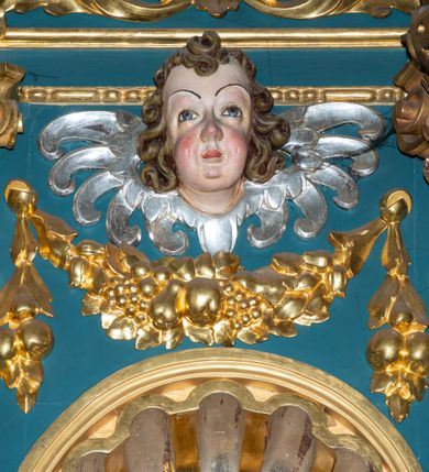 Zdjęcie nr 19: Ołtarz w kaplicy Matki Boskiej Szaflarskiej stanowi przykład przyściennej, architektonicznej, drewnianej nastawy trójosiowej ze zwieńczeniem. Stipes ołtarzowy z drewnianą mensą z kamiennym portatylem uzyskał kształt leżącego prostopadłościanu. Jego przód flankują hermy o trzonach dekorowanych cekinami. W polu zastosowano prostokątną płycinę ujętą kimationem. Na mensie ustawiono prostopadłościenne tabernakulum z wyodrębnionym cokołem i gzymsem koronującym wyłamanym na osi, podtrzymywanym przez dwa pilastry. Krawędzie tabernakulum zdobi imitacja boniowania. Drzwiczki ozdobiono stojącą, prostokątną płyciną, zwieńczoną trójkątnym przyczółkiem. W polu płyciny umieszczono stojący na obłokach płaskorzeźbiony i złocony kielich z hostią otoczoną promieniami. Jednokondygnacyjna nastawa wspiera się na prostokątnej predelli, przechodzącej pod osiami bocznymi w wolutowe konsole. Osie retabulum wydzielone zostały za pomocą skrajnych pilastrów oraz pary kolumn flankujących oś środkową. Podpory dźwigają pełne belkowanie wyłamane na ich osi, przerwane w partii pola środkowego oraz na osiach skrajnych przerwany półokrągły przyczółek. Wewnętrzna para kolumn dźwiga dodatkowo parę konsol podtrzymujących pełne belkowanie wyłamane na ich osi. Zwieńczenie uzyskało formę kwadratu zamkniętego szczytem z krzyżem, ujętego parą kolumienek na cokołach podtrzymujących skrajne woluty. Po zewnętrznych bokach zwieńczenia usytuowano postacie adorujących aniołów. W polu środkowym kondygnacji znalazła się nisza w formie stojącego prostokąta zamkniętego archiwoltą opadającą na belkowanie z konchą wydzieloną przez poziomy gzyms wsparty na dwóch pilastrach. W podniebiu konchy widoczna jest rzeźbiona i srebrzona gołębica Ducha Świętego. W niszy ustawiono figurę Matki Boskiej z Dzieciątkiem stojącą na wysokim czworobocznym postumencie. W osiach bocznych znalazły się nisze zamknięte konchą, u dołu podtrzymywane wspornikiem, z figurami św. Elżbiety Węgierskiej i św. Kazimierza Królewicza. W polu zwieńczenia umieszczono obraz w formie owalu ujęty ramą z przedstawieniem św. Maurycego. Ołtarz w całości pokryty został bogatą i zróżnicowaną dekoracją ornamentalną. Liśćmi akantu ozdobiono cokoły kolumn i wolut podwieszonych pod boczne osie. Kolumny w jednej czwartej wysokości obwiedzione zostały profilowaną listwą wypełnioną rautami. Ich dolne części ozdobiono uskrzydlonymi główkami aniołów z podwieszonymi festonami i girlandami. Z kolei w górnych partiach wykorzystano spiralne wici winnego grona. Dekoracyjnie artykułowano także pilastry, które w jednej czwartej przedzielono profilowanym gzymsem. Ich dolne części szczelnie wypełniono ornamentem okuciowym z rautem w środku, z kolei górne pokryto układającą się swobodnie i symetrycznie wstęgą z kaboszonami. Fryz belkowania wypełniony został wicią roślinną. Pola pomiędzy niszą a belkowaniem ozdobiono uskrzydlonymi główkami aniołów i podwieszonymi pod nimi girlandami. Ponadto uskrzydlone główki aniołów zdobią imposty podstawy zwieńczenia oraz klucz archiwolty ponad niszą główną. Kolumieńki zwieńczenia ozdobione zostały układającą się spiralnie wstęgą. Na dekoracje ornamentalną nastawy składają się również różne zdobienia profilów belkowania i zwieńczenia w postaci kostkowania, wolich oczu oraz pasów utworzonych z liści akantu.
