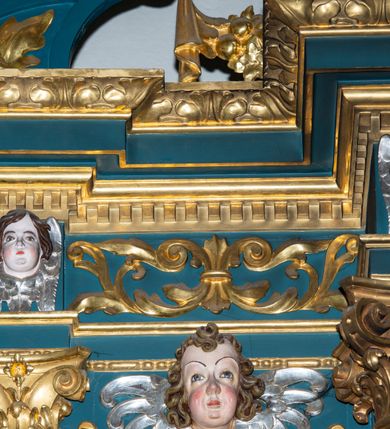 Zdjęcie nr 20: Ołtarz w kaplicy Matki Boskiej Szaflarskiej stanowi przykład przyściennej, architektonicznej, drewnianej nastawy trójosiowej ze zwieńczeniem. Stipes ołtarzowy z drewnianą mensą z kamiennym portatylem uzyskał kształt leżącego prostopadłościanu. Jego przód flankują hermy o trzonach dekorowanych cekinami. W polu zastosowano prostokątną płycinę ujętą kimationem. Na mensie ustawiono prostopadłościenne tabernakulum z wyodrębnionym cokołem i gzymsem koronującym wyłamanym na osi, podtrzymywanym przez dwa pilastry. Krawędzie tabernakulum zdobi imitacja boniowania. Drzwiczki ozdobiono stojącą, prostokątną płyciną, zwieńczoną trójkątnym przyczółkiem. W polu płyciny umieszczono stojący na obłokach płaskorzeźbiony i złocony kielich z hostią otoczoną promieniami. Jednokondygnacyjna nastawa wspiera się na prostokątnej predelli, przechodzącej pod osiami bocznymi w wolutowe konsole. Osie retabulum wydzielone zostały za pomocą skrajnych pilastrów oraz pary kolumn flankujących oś środkową. Podpory dźwigają pełne belkowanie wyłamane na ich osi, przerwane w partii pola środkowego oraz na osiach skrajnych przerwany półokrągły przyczółek. Wewnętrzna para kolumn dźwiga dodatkowo parę konsol podtrzymujących pełne belkowanie wyłamane na ich osi. Zwieńczenie uzyskało formę kwadratu zamkniętego szczytem z krzyżem, ujętego parą kolumienek na cokołach podtrzymujących skrajne woluty. Po zewnętrznych bokach zwieńczenia usytuowano postacie adorujących aniołów. W polu środkowym kondygnacji znalazła się nisza w formie stojącego prostokąta zamkniętego archiwoltą opadającą na belkowanie z konchą wydzieloną przez poziomy gzyms wsparty na dwóch pilastrach. W podniebiu konchy widoczna jest rzeźbiona i srebrzona gołębica Ducha Świętego. W niszy ustawiono figurę Matki Boskiej z Dzieciątkiem stojącą na wysokim czworobocznym postumencie. W osiach bocznych znalazły się nisze zamknięte konchą, u dołu podtrzymywane wspornikiem, z figurami św. Elżbiety Węgierskiej i św. Kazimierza Królewicza. W polu zwieńczenia umieszczono obraz w formie owalu ujęty ramą z przedstawieniem św. Maurycego. Ołtarz w całości pokryty został bogatą i zróżnicowaną dekoracją ornamentalną. Liśćmi akantu ozdobiono cokoły kolumn i wolut podwieszonych pod boczne osie. Kolumny w jednej czwartej wysokości obwiedzione zostały profilowaną listwą wypełnioną rautami. Ich dolne części ozdobiono uskrzydlonymi główkami aniołów z podwieszonymi festonami i girlandami. Z kolei w górnych partiach wykorzystano spiralne wici winnego grona. Dekoracyjnie artykułowano także pilastry, które w jednej czwartej przedzielono profilowanym gzymsem. Ich dolne części szczelnie wypełniono ornamentem okuciowym z rautem w środku, z kolei górne pokryto układającą się swobodnie i symetrycznie wstęgą z kaboszonami. Fryz belkowania wypełniony został wicią roślinną. Pola pomiędzy niszą a belkowaniem ozdobiono uskrzydlonymi główkami aniołów i podwieszonymi pod nimi girlandami. Ponadto uskrzydlone główki aniołów zdobią imposty podstawy zwieńczenia oraz klucz archiwolty ponad niszą główną. Kolumieńki zwieńczenia ozdobione zostały układającą się spiralnie wstęgą. Na dekoracje ornamentalną nastawy składają się również różne zdobienia profilów belkowania i zwieńczenia w postaci kostkowania, wolich oczu oraz pasów utworzonych z liści akantu.
