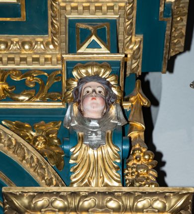 Zdjęcie nr 24: Ołtarz w kaplicy Matki Boskiej Szaflarskiej stanowi przykład przyściennej, architektonicznej, drewnianej nastawy trójosiowej ze zwieńczeniem. Stipes ołtarzowy z drewnianą mensą z kamiennym portatylem uzyskał kształt leżącego prostopadłościanu. Jego przód flankują hermy o trzonach dekorowanych cekinami. W polu zastosowano prostokątną płycinę ujętą kimationem. Na mensie ustawiono prostopadłościenne tabernakulum z wyodrębnionym cokołem i gzymsem koronującym wyłamanym na osi, podtrzymywanym przez dwa pilastry. Krawędzie tabernakulum zdobi imitacja boniowania. Drzwiczki ozdobiono stojącą, prostokątną płyciną, zwieńczoną trójkątnym przyczółkiem. W polu płyciny umieszczono stojący na obłokach płaskorzeźbiony i złocony kielich z hostią otoczoną promieniami. Jednokondygnacyjna nastawa wspiera się na prostokątnej predelli, przechodzącej pod osiami bocznymi w wolutowe konsole. Osie retabulum wydzielone zostały za pomocą skrajnych pilastrów oraz pary kolumn flankujących oś środkową. Podpory dźwigają pełne belkowanie wyłamane na ich osi, przerwane w partii pola środkowego oraz na osiach skrajnych przerwany półokrągły przyczółek. Wewnętrzna para kolumn dźwiga dodatkowo parę konsol podtrzymujących pełne belkowanie wyłamane na ich osi. Zwieńczenie uzyskało formę kwadratu zamkniętego szczytem z krzyżem, ujętego parą kolumienek na cokołach podtrzymujących skrajne woluty. Po zewnętrznych bokach zwieńczenia usytuowano postacie adorujących aniołów. W polu środkowym kondygnacji znalazła się nisza w formie stojącego prostokąta zamkniętego archiwoltą opadającą na belkowanie z konchą wydzieloną przez poziomy gzyms wsparty na dwóch pilastrach. W podniebiu konchy widoczna jest rzeźbiona i srebrzona gołębica Ducha Świętego. W niszy ustawiono figurę Matki Boskiej z Dzieciątkiem stojącą na wysokim czworobocznym postumencie. W osiach bocznych znalazły się nisze zamknięte konchą, u dołu podtrzymywane wspornikiem, z figurami św. Elżbiety Węgierskiej i św. Kazimierza Królewicza. W polu zwieńczenia umieszczono obraz w formie owalu ujęty ramą z przedstawieniem św. Maurycego. Ołtarz w całości pokryty został bogatą i zróżnicowaną dekoracją ornamentalną. Liśćmi akantu ozdobiono cokoły kolumn i wolut podwieszonych pod boczne osie. Kolumny w jednej czwartej wysokości obwiedzione zostały profilowaną listwą wypełnioną rautami. Ich dolne części ozdobiono uskrzydlonymi główkami aniołów z podwieszonymi festonami i girlandami. Z kolei w górnych partiach wykorzystano spiralne wici winnego grona. Dekoracyjnie artykułowano także pilastry, które w jednej czwartej przedzielono profilowanym gzymsem. Ich dolne części szczelnie wypełniono ornamentem okuciowym z rautem w środku, z kolei górne pokryto układającą się swobodnie i symetrycznie wstęgą z kaboszonami. Fryz belkowania wypełniony został wicią roślinną. Pola pomiędzy niszą a belkowaniem ozdobiono uskrzydlonymi główkami aniołów i podwieszonymi pod nimi girlandami. Ponadto uskrzydlone główki aniołów zdobią imposty podstawy zwieńczenia oraz klucz archiwolty ponad niszą główną. Kolumieńki zwieńczenia ozdobione zostały układającą się spiralnie wstęgą. Na dekoracje ornamentalną nastawy składają się również różne zdobienia profilów belkowania i zwieńczenia w postaci kostkowania, wolich oczu oraz pasów utworzonych z liści akantu.
