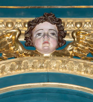 Zdjęcie nr 26: Ołtarz w kaplicy Matki Boskiej Szaflarskiej stanowi przykład przyściennej, architektonicznej, drewnianej nastawy trójosiowej ze zwieńczeniem. Stipes ołtarzowy z drewnianą mensą z kamiennym portatylem uzyskał kształt leżącego prostopadłościanu. Jego przód flankują hermy o trzonach dekorowanych cekinami. W polu zastosowano prostokątną płycinę ujętą kimationem. Na mensie ustawiono prostopadłościenne tabernakulum z wyodrębnionym cokołem i gzymsem koronującym wyłamanym na osi, podtrzymywanym przez dwa pilastry. Krawędzie tabernakulum zdobi imitacja boniowania. Drzwiczki ozdobiono stojącą, prostokątną płyciną, zwieńczoną trójkątnym przyczółkiem. W polu płyciny umieszczono stojący na obłokach płaskorzeźbiony i złocony kielich z hostią otoczoną promieniami. Jednokondygnacyjna nastawa wspiera się na prostokątnej predelli, przechodzącej pod osiami bocznymi w wolutowe konsole. Osie retabulum wydzielone zostały za pomocą skrajnych pilastrów oraz pary kolumn flankujących oś środkową. Podpory dźwigają pełne belkowanie wyłamane na ich osi, przerwane w partii pola środkowego oraz na osiach skrajnych przerwany półokrągły przyczółek. Wewnętrzna para kolumn dźwiga dodatkowo parę konsol podtrzymujących pełne belkowanie wyłamane na ich osi. Zwieńczenie uzyskało formę kwadratu zamkniętego szczytem z krzyżem, ujętego parą kolumienek na cokołach podtrzymujących skrajne woluty. Po zewnętrznych bokach zwieńczenia usytuowano postacie adorujących aniołów. W polu środkowym kondygnacji znalazła się nisza w formie stojącego prostokąta zamkniętego archiwoltą opadającą na belkowanie z konchą wydzieloną przez poziomy gzyms wsparty na dwóch pilastrach. W podniebiu konchy widoczna jest rzeźbiona i srebrzona gołębica Ducha Świętego. W niszy ustawiono figurę Matki Boskiej z Dzieciątkiem stojącą na wysokim czworobocznym postumencie. W osiach bocznych znalazły się nisze zamknięte konchą, u dołu podtrzymywane wspornikiem, z figurami św. Elżbiety Węgierskiej i św. Kazimierza Królewicza. W polu zwieńczenia umieszczono obraz w formie owalu ujęty ramą z przedstawieniem św. Maurycego. Ołtarz w całości pokryty został bogatą i zróżnicowaną dekoracją ornamentalną. Liśćmi akantu ozdobiono cokoły kolumn i wolut podwieszonych pod boczne osie. Kolumny w jednej czwartej wysokości obwiedzione zostały profilowaną listwą wypełnioną rautami. Ich dolne części ozdobiono uskrzydlonymi główkami aniołów z podwieszonymi festonami i girlandami. Z kolei w górnych partiach wykorzystano spiralne wici winnego grona. Dekoracyjnie artykułowano także pilastry, które w jednej czwartej przedzielono profilowanym gzymsem. Ich dolne części szczelnie wypełniono ornamentem okuciowym z rautem w środku, z kolei górne pokryto układającą się swobodnie i symetrycznie wstęgą z kaboszonami. Fryz belkowania wypełniony został wicią roślinną. Pola pomiędzy niszą a belkowaniem ozdobiono uskrzydlonymi główkami aniołów i podwieszonymi pod nimi girlandami. Ponadto uskrzydlone główki aniołów zdobią imposty podstawy zwieńczenia oraz klucz archiwolty ponad niszą główną. Kolumieńki zwieńczenia ozdobione zostały układającą się spiralnie wstęgą. Na dekoracje ornamentalną nastawy składają się również różne zdobienia profilów belkowania i zwieńczenia w postaci kostkowania, wolich oczu oraz pasów utworzonych z liści akantu.
