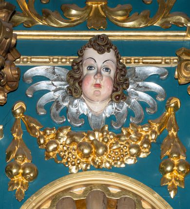 Zdjęcie nr 27: Ołtarz w kaplicy Matki Boskiej Szaflarskiej stanowi przykład przyściennej, architektonicznej, drewnianej nastawy trójosiowej ze zwieńczeniem. Stipes ołtarzowy z drewnianą mensą z kamiennym portatylem uzyskał kształt leżącego prostopadłościanu. Jego przód flankują hermy o trzonach dekorowanych cekinami. W polu zastosowano prostokątną płycinę ujętą kimationem. Na mensie ustawiono prostopadłościenne tabernakulum z wyodrębnionym cokołem i gzymsem koronującym wyłamanym na osi, podtrzymywanym przez dwa pilastry. Krawędzie tabernakulum zdobi imitacja boniowania. Drzwiczki ozdobiono stojącą, prostokątną płyciną, zwieńczoną trójkątnym przyczółkiem. W polu płyciny umieszczono stojący na obłokach płaskorzeźbiony i złocony kielich z hostią otoczoną promieniami. Jednokondygnacyjna nastawa wspiera się na prostokątnej predelli, przechodzącej pod osiami bocznymi w wolutowe konsole. Osie retabulum wydzielone zostały za pomocą skrajnych pilastrów oraz pary kolumn flankujących oś środkową. Podpory dźwigają pełne belkowanie wyłamane na ich osi, przerwane w partii pola środkowego oraz na osiach skrajnych przerwany półokrągły przyczółek. Wewnętrzna para kolumn dźwiga dodatkowo parę konsol podtrzymujących pełne belkowanie wyłamane na ich osi. Zwieńczenie uzyskało formę kwadratu zamkniętego szczytem z krzyżem, ujętego parą kolumienek na cokołach podtrzymujących skrajne woluty. Po zewnętrznych bokach zwieńczenia usytuowano postacie adorujących aniołów. W polu środkowym kondygnacji znalazła się nisza w formie stojącego prostokąta zamkniętego archiwoltą opadającą na belkowanie z konchą wydzieloną przez poziomy gzyms wsparty na dwóch pilastrach. W podniebiu konchy widoczna jest rzeźbiona i srebrzona gołębica Ducha Świętego. W niszy ustawiono figurę Matki Boskiej z Dzieciątkiem stojącą na wysokim czworobocznym postumencie. W osiach bocznych znalazły się nisze zamknięte konchą, u dołu podtrzymywane wspornikiem, z figurami św. Elżbiety Węgierskiej i św. Kazimierza Królewicza. W polu zwieńczenia umieszczono obraz w formie owalu ujęty ramą z przedstawieniem św. Maurycego. Ołtarz w całości pokryty został bogatą i zróżnicowaną dekoracją ornamentalną. Liśćmi akantu ozdobiono cokoły kolumn i wolut podwieszonych pod boczne osie. Kolumny w jednej czwartej wysokości obwiedzione zostały profilowaną listwą wypełnioną rautami. Ich dolne części ozdobiono uskrzydlonymi główkami aniołów z podwieszonymi festonami i girlandami. Z kolei w górnych partiach wykorzystano spiralne wici winnego grona. Dekoracyjnie artykułowano także pilastry, które w jednej czwartej przedzielono profilowanym gzymsem. Ich dolne części szczelnie wypełniono ornamentem okuciowym z rautem w środku, z kolei górne pokryto układającą się swobodnie i symetrycznie wstęgą z kaboszonami. Fryz belkowania wypełniony został wicią roślinną. Pola pomiędzy niszą a belkowaniem ozdobiono uskrzydlonymi główkami aniołów i podwieszonymi pod nimi girlandami. Ponadto uskrzydlone główki aniołów zdobią imposty podstawy zwieńczenia oraz klucz archiwolty ponad niszą główną. Kolumieńki zwieńczenia ozdobione zostały układającą się spiralnie wstęgą. Na dekoracje ornamentalną nastawy składają się również różne zdobienia profilów belkowania i zwieńczenia w postaci kostkowania, wolich oczu oraz pasów utworzonych z liści akantu.
