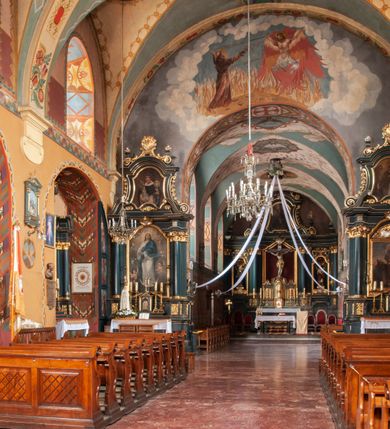 Zdjęcie nr 11: Kościół jest położony na wzgórzu w pobliżu centrum, przy ul. Brata Alojzego Kosiby. Od zachodu przed kościołem znajduje się dziedziniec i dawny cmentarz obwiedzione murem z bramkami i stacjami Męki Pańskiej. Z cmentarza wejście prowadzi do kościoła, a przez furtę na teren przyklasztorny i dalej do ogrodu klasztornego. Kościół wzniesiony jest z cegły, otynkowany. Świątynia jest orientowana, jednonawowa, z węższym prezbiterium, z kaplicą od północy i kruchtą od zachodu. Przy kościele od południa znajdują się zakrystia i zabudowania klasztorne. Prezbiterium na rzucie prostokąta, zamknięte od wschodu prostą ścianą, trójprzęsłowe, przekryte sklepieniem kolebkowym z przecinającymi się lunetami. W każdym przęśle ściany północnej wysoko umieszczone półkoliście zamknięte okna. Otworom okiennym odpowiadają tej samej wielkości nisze umieszczone w ścianie południowej. Wejście do klasztornego korytarza i zakrystii umieszczone jest w przęśle środkowym. Odpowiada mu otwór komunikacyjny po stronie przeciwnej. W przęśle zachodnim zlokalizowano drugie wejście do południowego korytarza klasztornego. Przestrzeń miedzy prezbiterium a korpusem zawężona arkadą tęczową, zamkniętą półkoliście. Korpus jednonawowy, szerszy z wnękami na ołtarze, czteroprzęsłowy, przekryty sklepieniem kolebkowym na gurtach z lunetami. Wnęka w trzecim przęśle od wschodu zamieniona na otwór do kaplicy północnej. Połowę przęsła zachodniego zajmuje empora muzyczna oparta na nisko schodzącym sklepieniu kolebkowym. Przy emporze, w ścianach wzdłużnych nawy, znacznie mniejsze, półkoliście zamknięte wnęki na konfesjonały. W lunetach, po obu stronach półkoliście zamknięte okna. Okna w przęśle zachodnim zastępują tej samej wielkości nisze. Główne wejście do kościoła w osi ściany zachodniej, zamknięte łukiem odcinkowym. W osi nad chórem muzycznym, półkoliście zamknięte okno, większe od pozostałych. Wejście do kościoła objęte prostokątnym portalem z piaskowca. Kaplica północna wzniesiona na planie kwadratu, przekryta sklepieniem współczesnym, zbliżonym w formie do klasztornego, zwieńczona latarnią. Okna, umieszczone w ścianie wschodniej i zachodniej, o tym samym wykroju utworzonym z wąskiego prostokąta przechodzącego górą w formę wachlarza lub wycinka koła. Zewnętrzne elewacje artykułuje podział osiowy i dekoracja lizenowo-ramowa, złożona z wydatnych elementów wertykalnych i horyzontalnych. Jednoosiową fasadę nad kruchtą ozdabia poniżej okna profilowany gzyms. Całość zamknięta wysoką, trójkątną ścianą szczytową, z trzema półkoliście zamkniętymi niszami. W nich polichromowane płaskorzeźby o kształcie stojącego prostokąta zamkniętego łukiem pełnym przedstawiające: stygmatyzację św. Franciszka, św. Piotra z Alkantary, św. Antoniego Padewskiego. Szczyt zwieńczony metalowym krzyżem osadzonym na niskim cokole. Kruchta przy fasadzie  z dwoma wejściami. Wejście zachodnie obejmuje półkoliście zamknięty portal z piaskowca, z dekoracją płycinową na węgarach, z kapitelami i skromnie profilowaną archiwoltą spiętą kluczem. Węższe wejście od północy z prostym, półkoliście zamkniętym portalem z piaskowca. Budowlę zamkniętą profilowanym gzymsem wieńczy trójkątny naczółek, przechodzący po bokach w balustradę z dekoracją płycinową. Na narożnych słupkach balustrady obeliskowe sterczyny. W półkoliście zamkniętej wnęce, umieszczonej pośrodku naczółka, wizerunek Matki Boskiej Nieustającej Pomocy. Wschodnia ściana prezbiterium, w dolnej partii zupełnie płaska, w górnej z triadą prostokątnych wnęk. Część szczytową oddziela od dolnej profilowany gzyms kryty dachówką. W osi trójkątnego szczytu wschodniego prostokątna wnęka z płaskorzeźbioną i polichromowaną sceną przedstawiającą św. Porcjunkulę w towarzystwie Chrystusa oraz św. Franciszka. Bryłę świątyni zamykają wysokie dachy dwuspadowe. Pośrodku dachu prezbiterium wieloboczna wieżyczka na sygnaturkę z ażurową latarnią. Bryłę kaplicy przekrywa dach czterospadowy. Ośmioboczną formę jej latarni zamyka dach wielospadowy zwieńczony metalowym krzyżem.