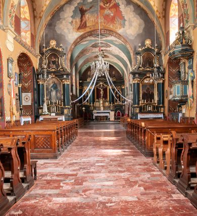 Zdjęcie nr 14: Kościół jest położony na wzgórzu w pobliżu centrum, przy ul. Brata Alojzego Kosiby. Od zachodu przed kościołem znajduje się dziedziniec i dawny cmentarz obwiedzione murem z bramkami i stacjami Męki Pańskiej. Z cmentarza wejście prowadzi do kościoła, a przez furtę na teren przyklasztorny i dalej do ogrodu klasztornego. Kościół wzniesiony jest z cegły, otynkowany. Świątynia jest orientowana, jednonawowa, z węższym prezbiterium, z kaplicą od północy i kruchtą od zachodu. Przy kościele od południa znajdują się zakrystia i zabudowania klasztorne. Prezbiterium na rzucie prostokąta, zamknięte od wschodu prostą ścianą, trójprzęsłowe, przekryte sklepieniem kolebkowym z przecinającymi się lunetami. W każdym przęśle ściany północnej wysoko umieszczone półkoliście zamknięte okna. Otworom okiennym odpowiadają tej samej wielkości nisze umieszczone w ścianie południowej. Wejście do klasztornego korytarza i zakrystii umieszczone jest w przęśle środkowym. Odpowiada mu otwór komunikacyjny po stronie przeciwnej. W przęśle zachodnim zlokalizowano drugie wejście do południowego korytarza klasztornego. Przestrzeń miedzy prezbiterium a korpusem zawężona arkadą tęczową, zamkniętą półkoliście. Korpus jednonawowy, szerszy z wnękami na ołtarze, czteroprzęsłowy, przekryty sklepieniem kolebkowym na gurtach z lunetami. Wnęka w trzecim przęśle od wschodu zamieniona na otwór do kaplicy północnej. Połowę przęsła zachodniego zajmuje empora muzyczna oparta na nisko schodzącym sklepieniu kolebkowym. Przy emporze, w ścianach wzdłużnych nawy, znacznie mniejsze, półkoliście zamknięte wnęki na konfesjonały. W lunetach, po obu stronach półkoliście zamknięte okna. Okna w przęśle zachodnim zastępują tej samej wielkości nisze. Główne wejście do kościoła w osi ściany zachodniej, zamknięte łukiem odcinkowym. W osi nad chórem muzycznym, półkoliście zamknięte okno, większe od pozostałych. Wejście do kościoła objęte prostokątnym portalem z piaskowca. Kaplica północna wzniesiona na planie kwadratu, przekryta sklepieniem współczesnym, zbliżonym w formie do klasztornego, zwieńczona latarnią. Okna, umieszczone w ścianie wschodniej i zachodniej, o tym samym wykroju utworzonym z wąskiego prostokąta przechodzącego górą w formę wachlarza lub wycinka koła. Zewnętrzne elewacje artykułuje podział osiowy i dekoracja lizenowo-ramowa, złożona z wydatnych elementów wertykalnych i horyzontalnych. Jednoosiową fasadę nad kruchtą ozdabia poniżej okna profilowany gzyms. Całość zamknięta wysoką, trójkątną ścianą szczytową, z trzema półkoliście zamkniętymi niszami. W nich polichromowane płaskorzeźby o kształcie stojącego prostokąta zamkniętego łukiem pełnym przedstawiające: stygmatyzację św. Franciszka, św. Piotra z Alkantary, św. Antoniego Padewskiego. Szczyt zwieńczony metalowym krzyżem osadzonym na niskim cokole. Kruchta przy fasadzie  z dwoma wejściami. Wejście zachodnie obejmuje półkoliście zamknięty portal z piaskowca, z dekoracją płycinową na węgarach, z kapitelami i skromnie profilowaną archiwoltą spiętą kluczem. Węższe wejście od północy z prostym, półkoliście zamkniętym portalem z piaskowca. Budowlę zamkniętą profilowanym gzymsem wieńczy trójkątny naczółek, przechodzący po bokach w balustradę z dekoracją płycinową. Na narożnych słupkach balustrady obeliskowe sterczyny. W półkoliście zamkniętej wnęce, umieszczonej pośrodku naczółka, wizerunek Matki Boskiej Nieustającej Pomocy. Wschodnia ściana prezbiterium, w dolnej partii zupełnie płaska, w górnej z triadą prostokątnych wnęk. Część szczytową oddziela od dolnej profilowany gzyms kryty dachówką. W osi trójkątnego szczytu wschodniego prostokątna wnęka z płaskorzeźbioną i polichromowaną sceną przedstawiającą św. Porcjunkulę w towarzystwie Chrystusa oraz św. Franciszka. Bryłę świątyni zamykają wysokie dachy dwuspadowe. Pośrodku dachu prezbiterium wieloboczna wieżyczka na sygnaturkę z ażurową latarnią. Bryłę kaplicy przekrywa dach czterospadowy. Ośmioboczną formę jej latarni zamyka dach wielospadowy zwieńczony metalowym krzyżem.