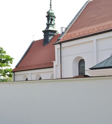 Zdjęcie nr 5: Kościół jest położony na wzgórzu w pobliżu centrum, przy ul. Brata Alojzego Kosiby. Od zachodu przed kościołem znajduje się dziedziniec i dawny cmentarz obwiedzione murem z bramkami i stacjami Męki Pańskiej. Z cmentarza wejście prowadzi do kościoła, a przez furtę na teren przyklasztorny i dalej do ogrodu klasztornego. Kościół wzniesiony jest z cegły, otynkowany. Świątynia jest orientowana, jednonawowa, z węższym prezbiterium, z kaplicą od północy i kruchtą od zachodu. Przy kościele od południa znajdują się zakrystia i zabudowania klasztorne. Prezbiterium na rzucie prostokąta, zamknięte od wschodu prostą ścianą, trójprzęsłowe, przekryte sklepieniem kolebkowym z przecinającymi się lunetami. W każdym przęśle ściany północnej wysoko umieszczone półkoliście zamknięte okna. Otworom okiennym odpowiadają tej samej wielkości nisze umieszczone w ścianie południowej. Wejście do klasztornego korytarza i zakrystii umieszczone jest w przęśle środkowym. Odpowiada mu otwór komunikacyjny po stronie przeciwnej. W przęśle zachodnim zlokalizowano drugie wejście do południowego korytarza klasztornego. Przestrzeń miedzy prezbiterium a korpusem zawężona arkadą tęczową, zamkniętą półkoliście. Korpus jednonawowy, szerszy z wnękami na ołtarze, czteroprzęsłowy, przekryty sklepieniem kolebkowym na gurtach z lunetami. Wnęka w trzecim przęśle od wschodu zamieniona na otwór do kaplicy północnej. Połowę przęsła zachodniego zajmuje empora muzyczna oparta na nisko schodzącym sklepieniu kolebkowym. Przy emporze, w ścianach wzdłużnych nawy, znacznie mniejsze, półkoliście zamknięte wnęki na konfesjonały. W lunetach, po obu stronach półkoliście zamknięte okna. Okna w przęśle zachodnim zastępują tej samej wielkości nisze. Główne wejście do kościoła w osi ściany zachodniej, zamknięte łukiem odcinkowym. W osi nad chórem muzycznym, półkoliście zamknięte okno, większe od pozostałych. Wejście do kościoła objęte prostokątnym portalem z piaskowca. Kaplica północna wzniesiona na planie kwadratu, przekryta sklepieniem współczesnym, zbliżonym w formie do klasztornego, zwieńczona latarnią. Okna, umieszczone w ścianie wschodniej i zachodniej, o tym samym wykroju utworzonym z wąskiego prostokąta przechodzącego górą w formę wachlarza lub wycinka koła. Zewnętrzne elewacje artykułuje podział osiowy i dekoracja lizenowo-ramowa, złożona z wydatnych elementów wertykalnych i horyzontalnych. Jednoosiową fasadę nad kruchtą ozdabia poniżej okna profilowany gzyms. Całość zamknięta wysoką, trójkątną ścianą szczytową, z trzema półkoliście zamkniętymi niszami. W nich polichromowane płaskorzeźby o kształcie stojącego prostokąta zamkniętego łukiem pełnym przedstawiające: stygmatyzację św. Franciszka, św. Piotra z Alkantary, św. Antoniego Padewskiego. Szczyt zwieńczony metalowym krzyżem osadzonym na niskim cokole. Kruchta przy fasadzie  z dwoma wejściami. Wejście zachodnie obejmuje półkoliście zamknięty portal z piaskowca, z dekoracją płycinową na węgarach, z kapitelami i skromnie profilowaną archiwoltą spiętą kluczem. Węższe wejście od północy z prostym, półkoliście zamkniętym portalem z piaskowca. Budowlę zamkniętą profilowanym gzymsem wieńczy trójkątny naczółek, przechodzący po bokach w balustradę z dekoracją płycinową. Na narożnych słupkach balustrady obeliskowe sterczyny. W półkoliście zamkniętej wnęce, umieszczonej pośrodku naczółka, wizerunek Matki Boskiej Nieustającej Pomocy. Wschodnia ściana prezbiterium, w dolnej partii zupełnie płaska, w górnej z triadą prostokątnych wnęk. Część szczytową oddziela od dolnej profilowany gzyms kryty dachówką. W osi trójkątnego szczytu wschodniego prostokątna wnęka z płaskorzeźbioną i polichromowaną sceną przedstawiającą św. Porcjunkulę w towarzystwie Chrystusa oraz św. Franciszka. Bryłę świątyni zamykają wysokie dachy dwuspadowe. Pośrodku dachu prezbiterium wieloboczna wieżyczka na sygnaturkę z ażurową latarnią. Bryłę kaplicy przekrywa dach czterospadowy. Ośmioboczną formę jej latarni zamyka dach wielospadowy zwieńczony metalowym krzyżem.