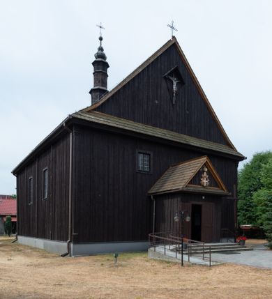 Zdjęcie nr 1: Kościół z drewna modrzewiowego o konstrukcji zrębowej, na betonowej podmurówce, otoczony drewnianym ogrodzeniem. Bryła składa się z korpusu nawowego na planie prostokąta oraz z wydłużonego, prostokątnego prezbiterium z zakrystią na przedłużeniu, węższego od nawy, zakończonego ścianą prostą, skierowanego na południe. Od strony północnej dobudowana jest prostokątna kruchta, od zachodu dwa przedsionki na dwóch skrajnych bokach –  przy nawie i prezbiterium. 
Trójprzęsłowe prezbiterium nakryte jest  sklepieniem pozornym zwierciadlanym, które przedłuża się nad nawę środkową. Ściany prezbiterium artykułowane pilastrami dzielą je na trzy przęsła. Kapitele pilastrów dźwigają nasadniki, które podtrzymują gzymsik. Przedłużeniem kapiteli w strefie stropu są płaskie belki biegnące przez całą jego szerokość, wyznaczając tym samym pola, w których umieszczono polichromię. Po obu stronach ołtarza drzwi w kształcie stojącego prostokąta. Prezbiterium od korpusu nawowego oddzielone silnie wystającą belką sklepienia oraz belką tęczową z grupą Ukrzyżowania. 
Korpus o trzech nawach o układzie halowym, z których środkowa jest dwa razy szersza od bocznych, trójprzęsłowa, z nawami oddzielonymi kanelowanymi filarami z nasadnikami podtrzymującymi gzyms. Nawy boczne nakryte kolebką. Na linii filarów pilastry na ścianach, łączą je poprzeczne belki sklepienia. W ostatnim przęśle chór muzyczny wsparty na dwóch filarach, z pełnym parapetem występującym w części środkowej trójbocznie do przodu. Jego krawędź dolna dekorowana jest lambrekinem. Ściany kościoła pokryte polichormią, pomalowane na jasnożółto, z jasnozielonymi podporami i brązowymi liniami podziału stropu. Te elementy wyznaczają ramy wypełnione polami z dekoracją ornamentalną w kształcie prostokątów i scenami figuralnymi zamkniętymi w kołach. 
Otwory okienne w drugim i trzecim przęśle nawy, od wschodu i zachodu, prostokątne. Także w prezbiterium po jednym prostokątnym oknie z każdej strony. Od strony wejścia dwa niewielkie okna prostokątne ponad kruchtą. Na ścianie zamknięcia zakrystii cztery prostokątne, symetrycznie rozłożone okna. 
 Fasada poprzedzona przedsionkiem w kształcie prostopadłościanu nakrytego dachem dwuspadowym, z przyczółkiem. Otwór drzwiowy w formie stojącego prostokąta, a w szczycie przyczółka trójkątne, wielodzielne okienko. Fasada w kształcie leżącego prostokąta z trójkątnym szczytem, części oddzielone daszkiem pulpitowym. Po dwóch stronach przedsionka prostokątne okna, w szczycie fasady  nakryty daszkiem krucyfiks. 
Elewacje zewnętrzne na podmurówce, artykułowane jedynie pionowymi, wystającymi przed lico belkami, przeprute oknami. Nad nawą i prezbiterium dachy dwuspadowe, nad prezbiterium niższy niż nad nawą, kryty blachą. Nad nawą wieżyczka na sygnaturkę zwieńczona cebulastym hełmem i krzyżem na szczycie. Na końcach dachu przy prezbiterium i nawie metalowe krzyże. 
